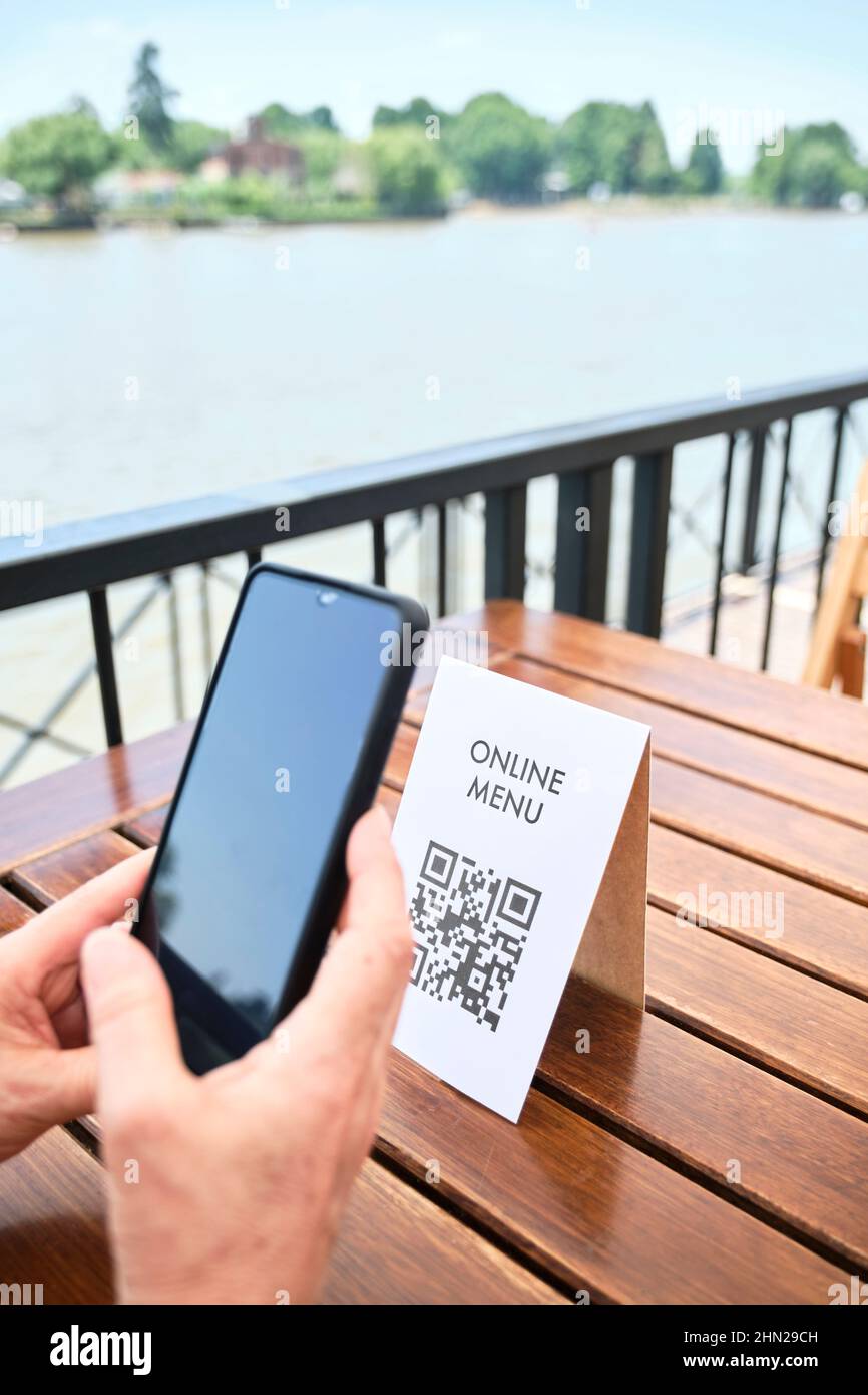 Hands of an unrecognizable woman scanning a QR code with a smartphone to access a restaurant menu; use of contactless technology in everyday life. Stock Photo