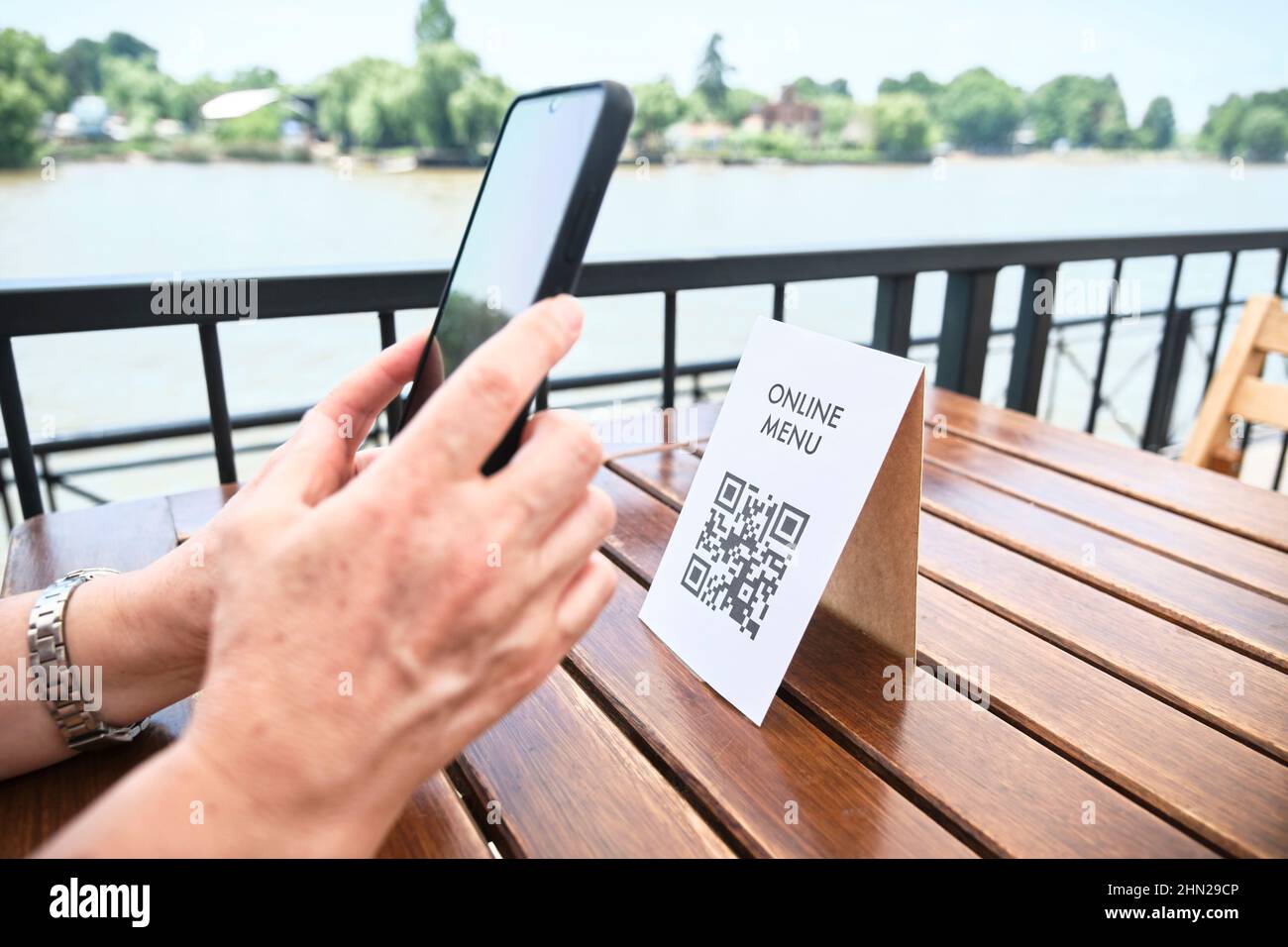 Hands of an unrecognizable woman scanning a QR code with a smartphone to access a restaurant menu; use of contactless technology in everyday life. Out Stock Photo