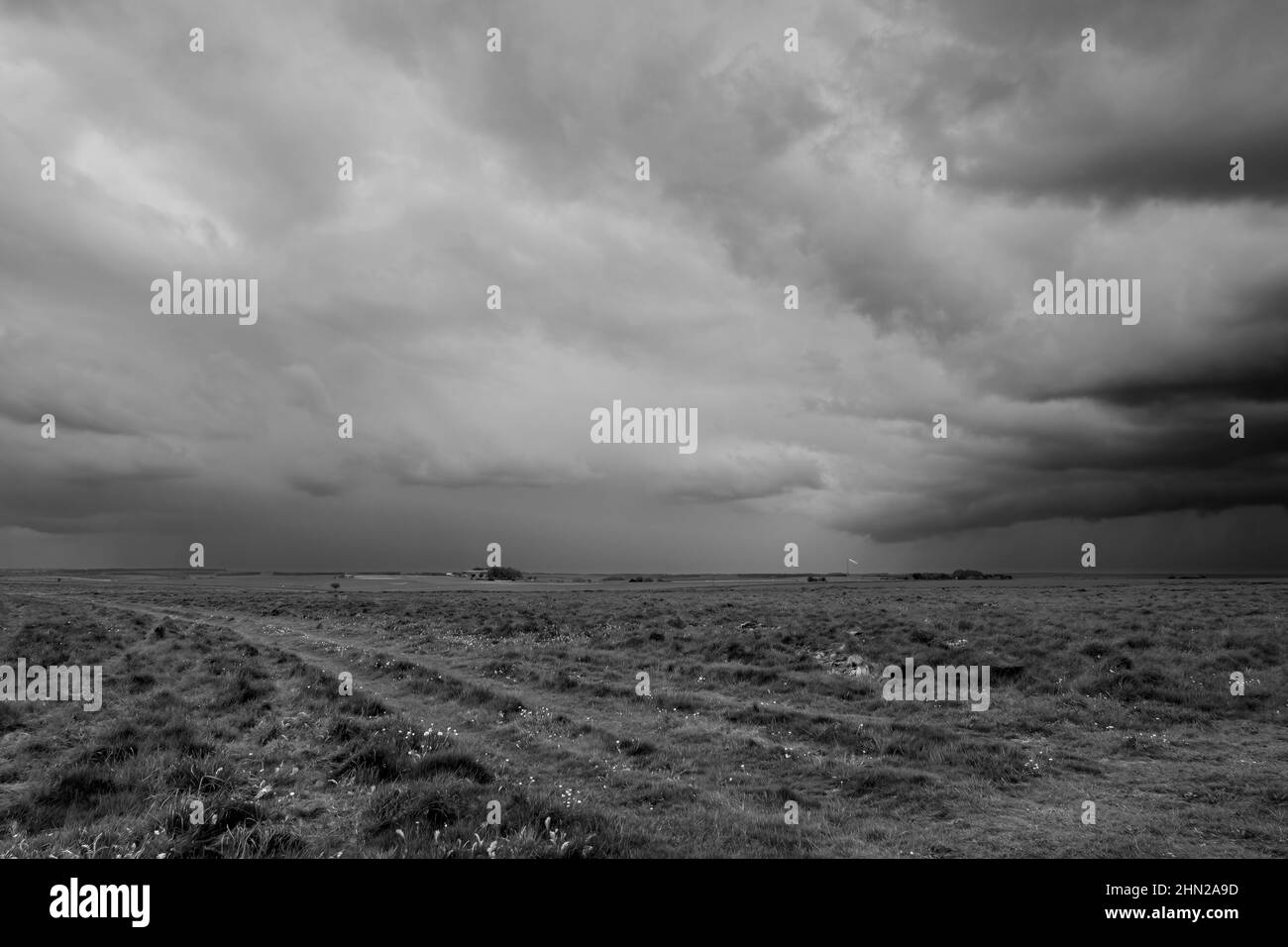 a foreboding dramatic dark grey thunder storm cloud sky over an open grass airfield and green meadows Stock Photo
