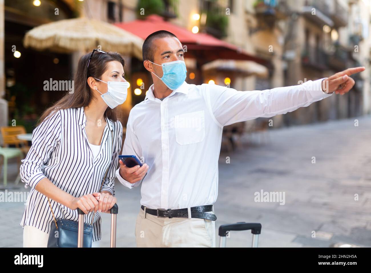 Couple of travelers in medical masks pointing at sights in foreign city ...