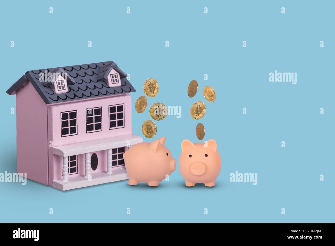 Couple in love, two piggy bank with golden Bitcons and wooden house on a bright blue background. Creative concept idea saving money for first house or Stock Photo