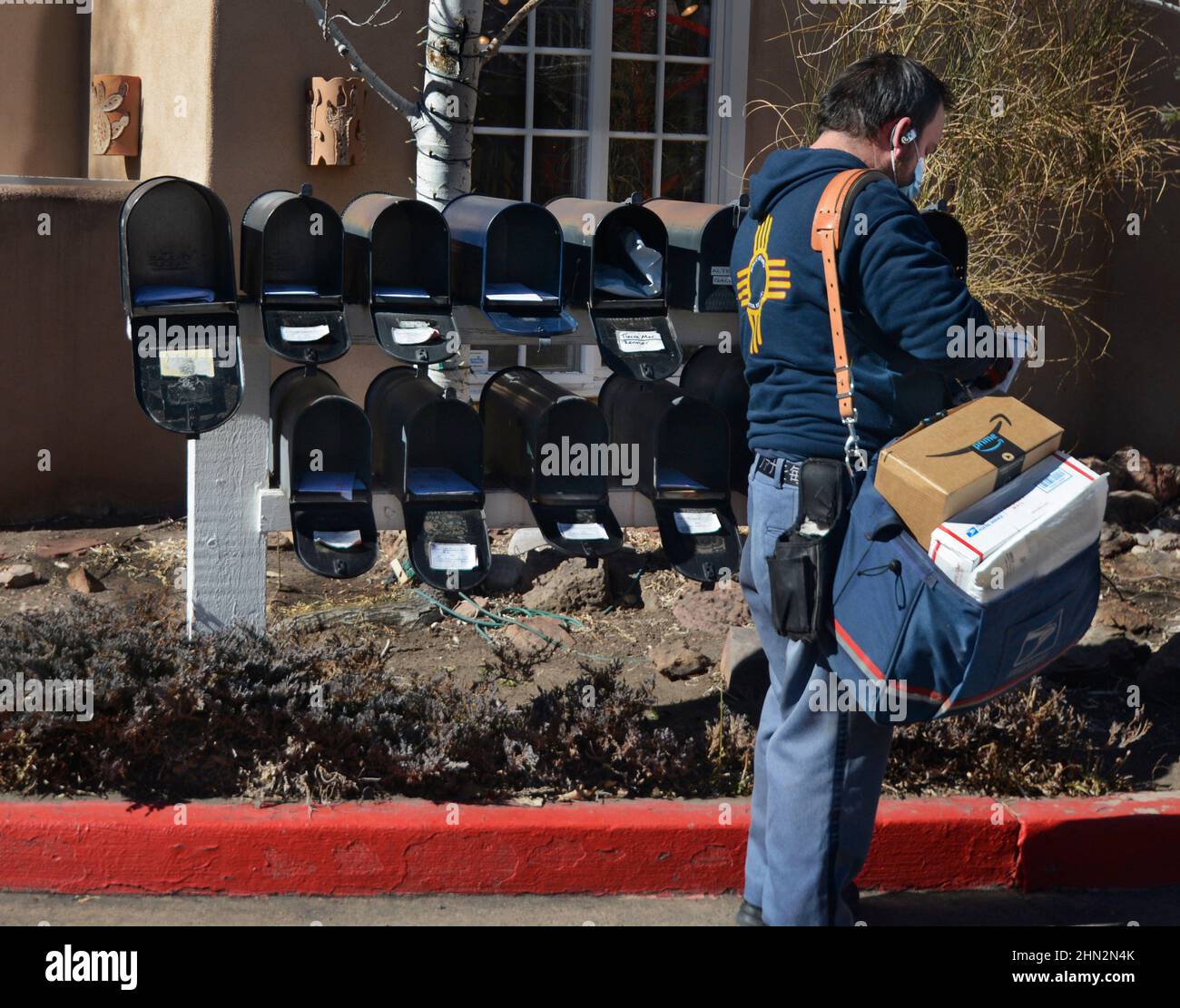 A mailman or letter carrier delivers mail to a row of mailboxes in Santa Fe, New Mexico. Stock Photo