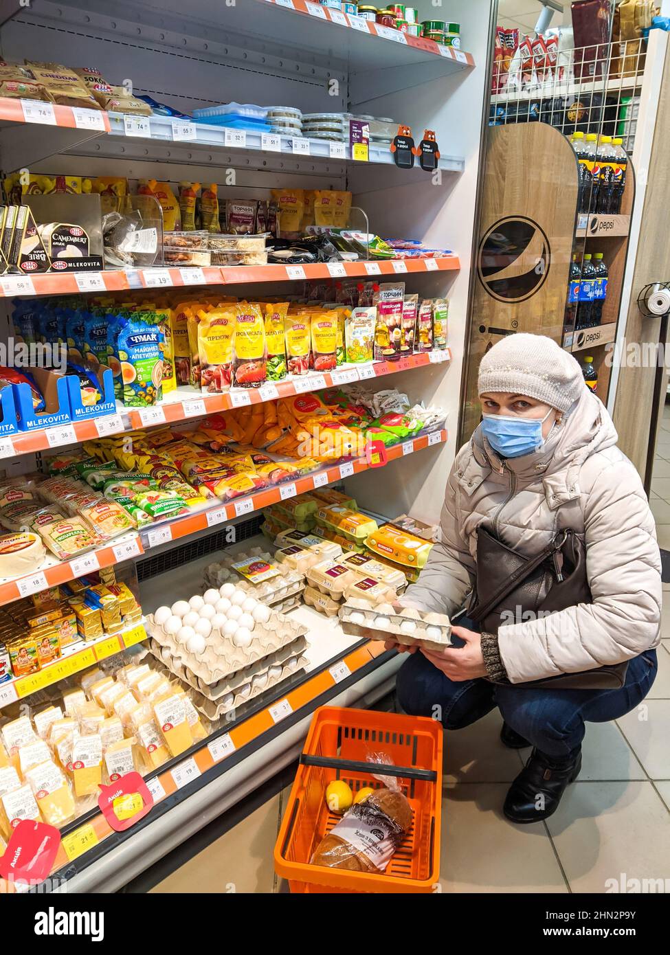 Volodymyr, Ukraine - 13.02.2022: woman choosing eggs in supermarket with different products. Supermarket aisle with colorful shelves of merchandise. R Stock Photo