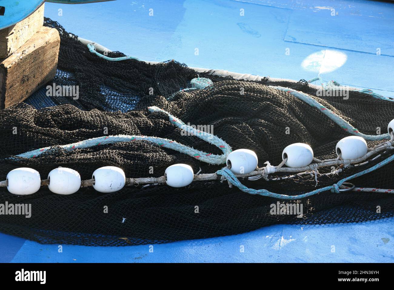 Small white buoys on black fishing netting against a blue background. Stock Photo