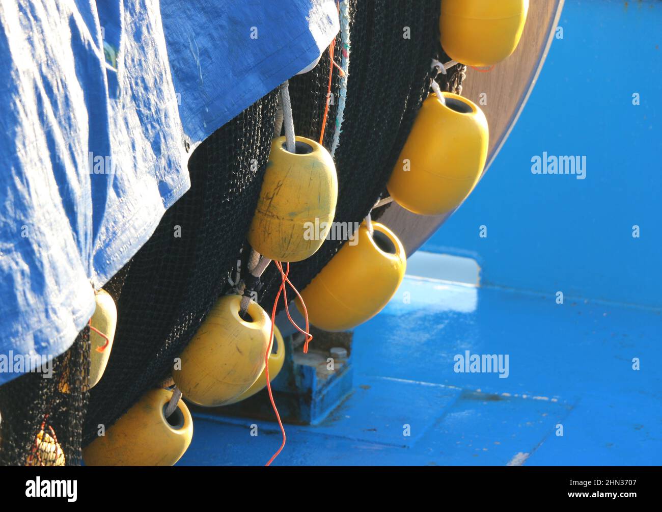 Bright yellow buoys hang from black netting against a background of shiny blue metal. Stock Photo
