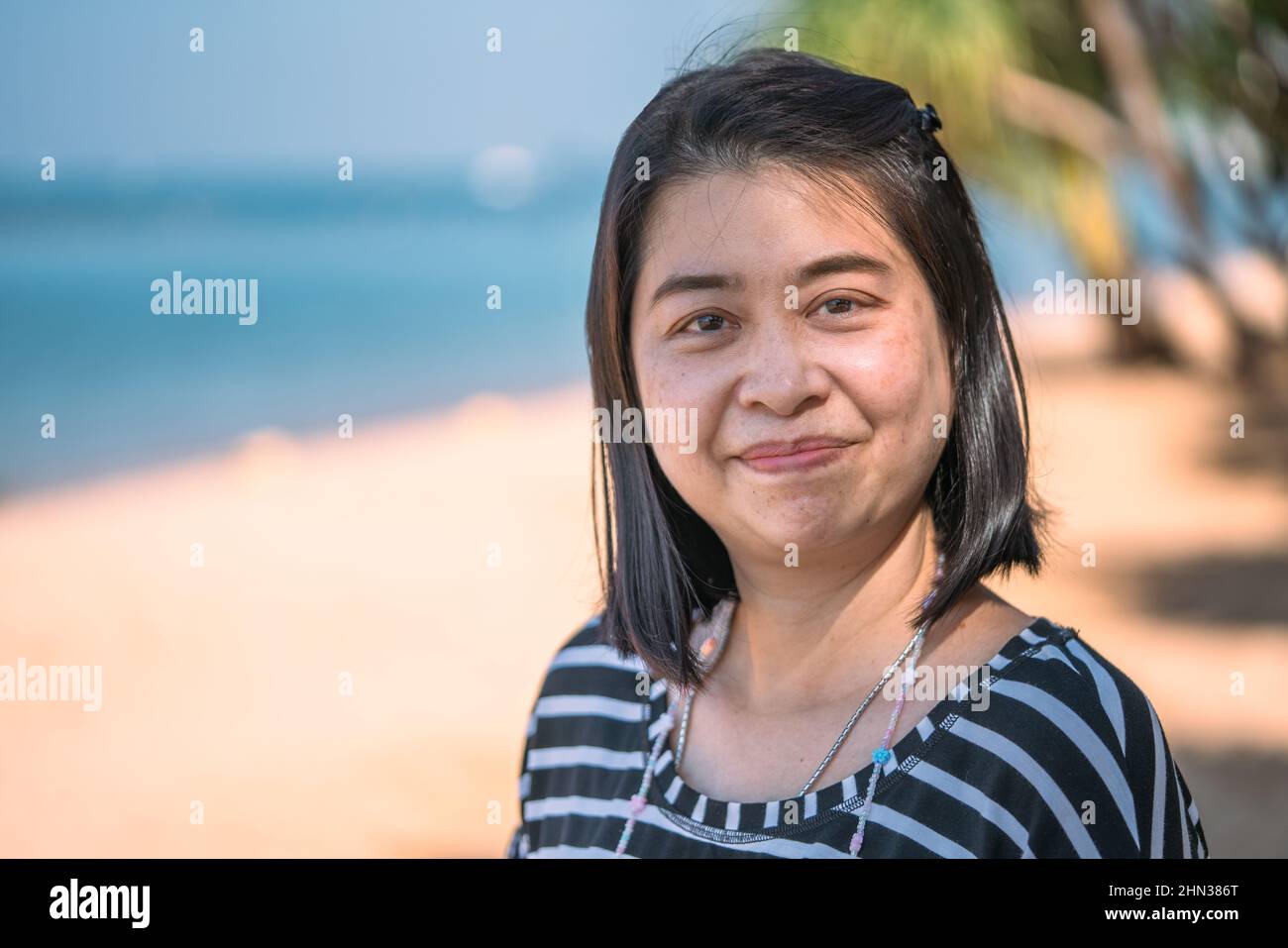 Portrait of Asian middle-aged woman on the beach, happy face with smiling face, natural skin without make up, show freckle, blemish on skin. Blurred b Stock Photo