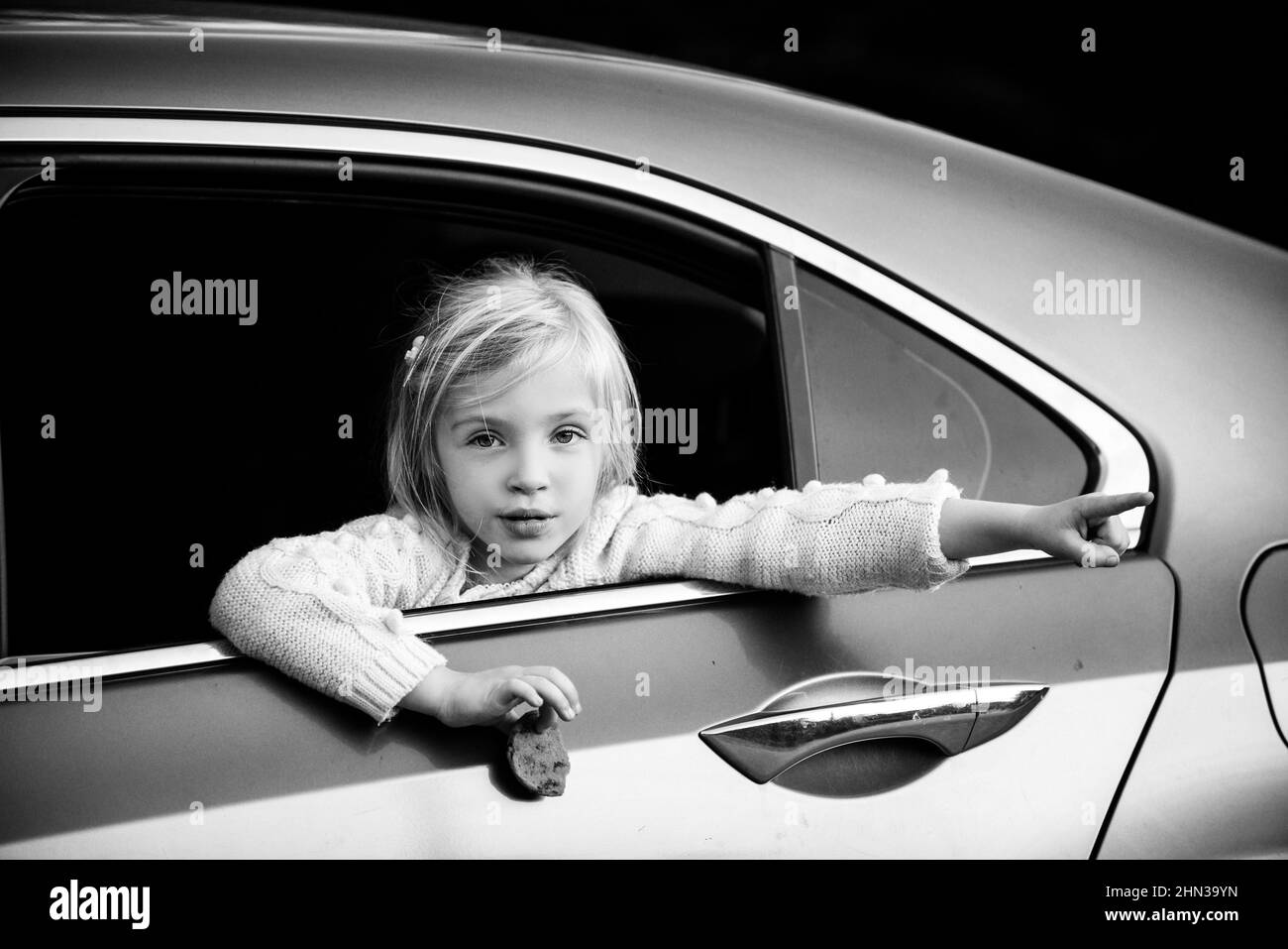 Little girl looks out the window in the car and something shows a hand. Stock Photo