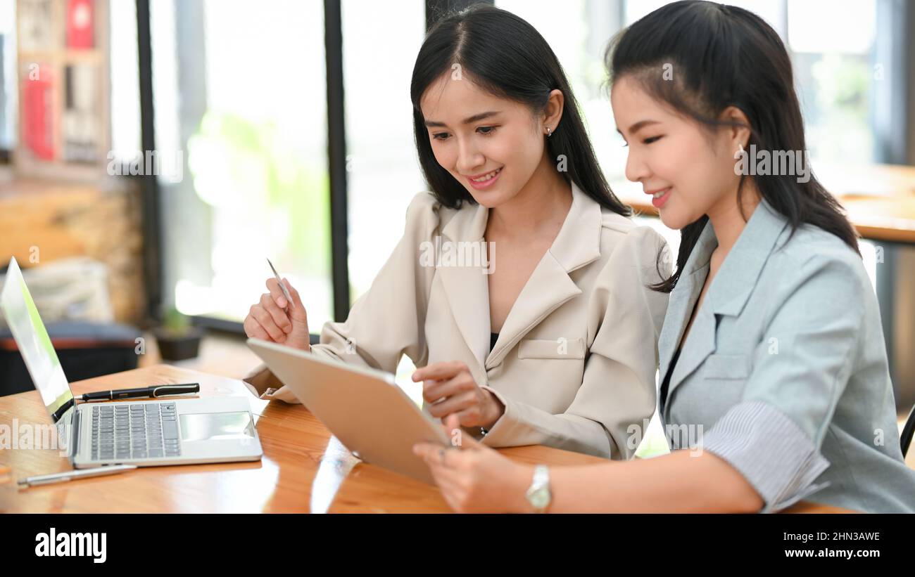 Two beautiful asian female business trainee are sharing their idea, planning the project, working and searching information on tablet together. Stock Photo