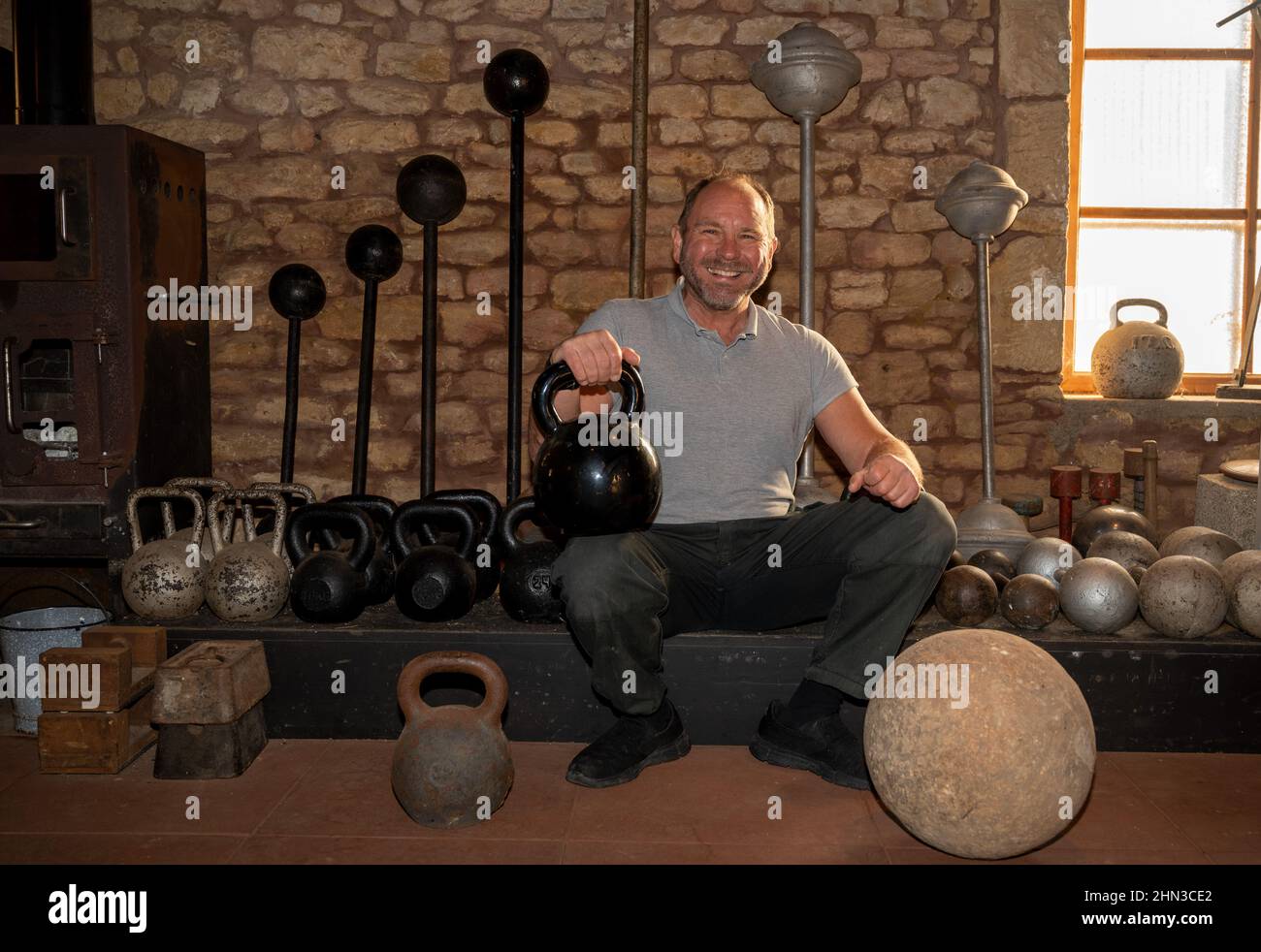 Luxemburg, Luxembourg. 09th Feb, 2021. Georges Christen squats in front of historic dumbbells and weights in his training barn. The Luxembourger is one of the strongest men in the world: he has 26 entries in the Guinness Book of Records. In just a few seconds, he tears up telephone books or bends thick nails. (to dpa: Georges Christen: The man who rolls up pans) Credit: Harald Tittel/dpa/Alamy Live News Stock Photo