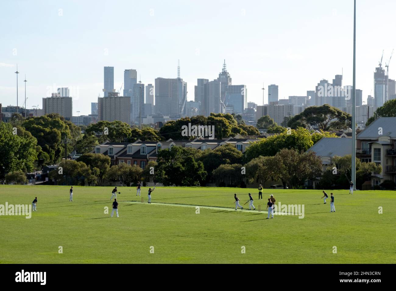 Young men playing cricket on the Ramsden Street oval in front of the Melbourne skyline in Clifton Hill, Melbourne, Victoria, Australia. Stock Photo