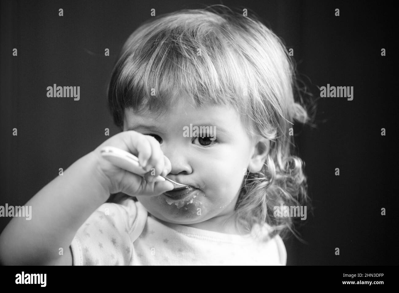 Baby eating with dirty face. Cheerful smiling child child eats itself with a spoon Baby eating