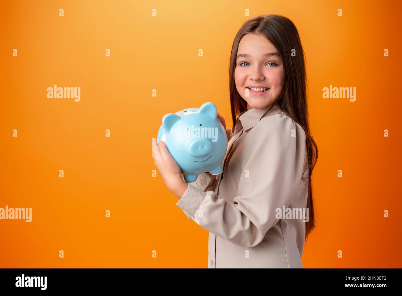Teen girl with piggy bank on orange color background Stock Photo - Alamy