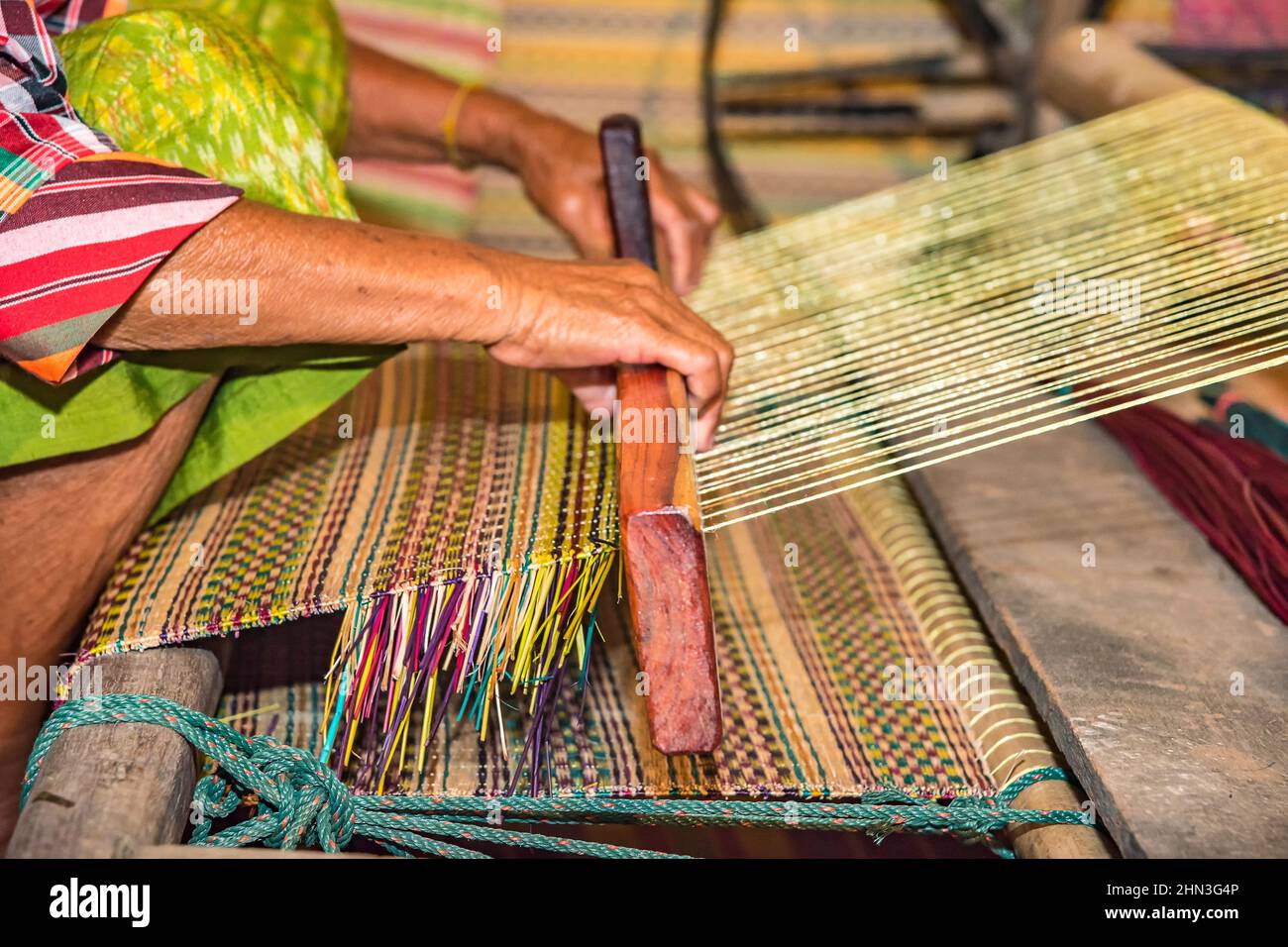 Closeup old woman hands weaving mats from dry reed. Stock Photo