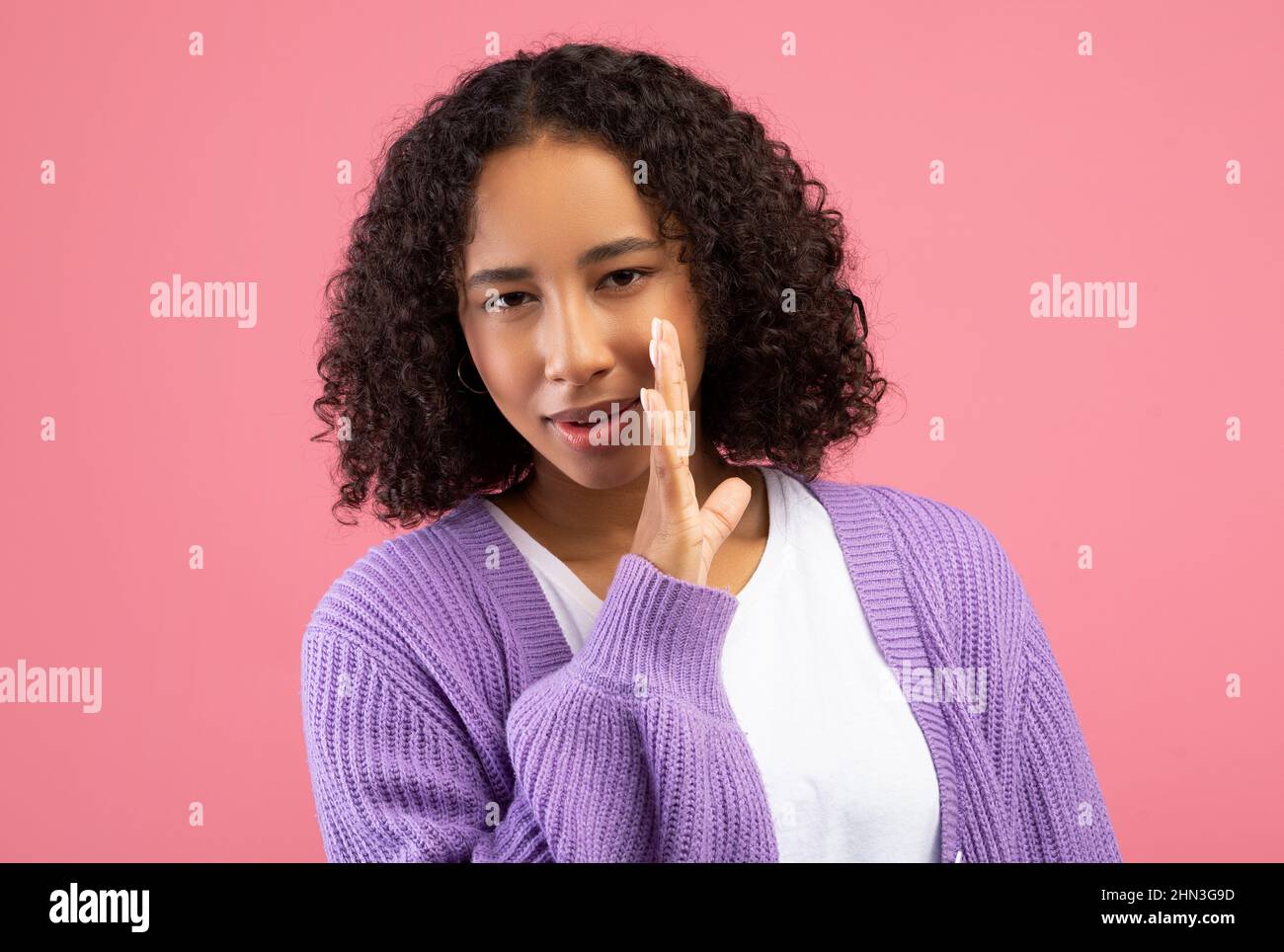 Young black woman whispering secret, sharing confidential information, spreading gossip on pink studio background Stock Photo