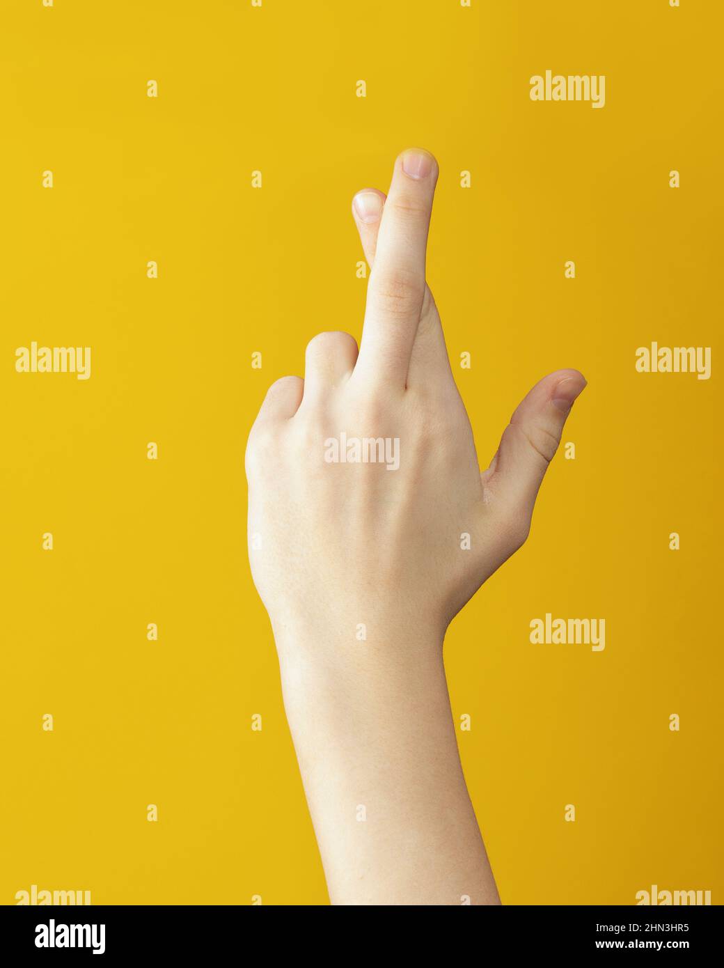 finger crossed hand sign on yellow background. Luck and superstitious concept. Stock Photo