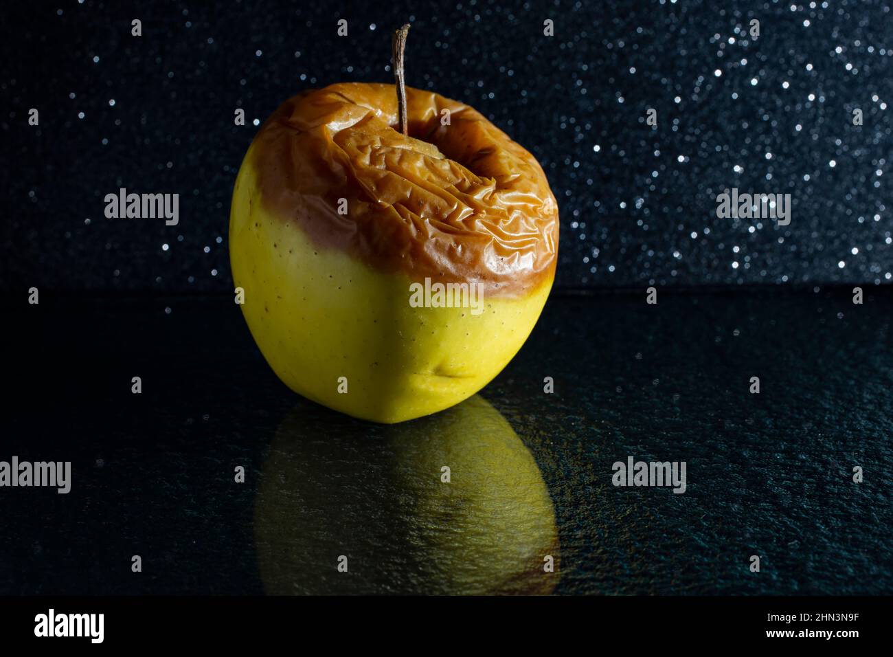 moody portrait of an rotten green  apple, on dark background with glass reflection Stock Photo