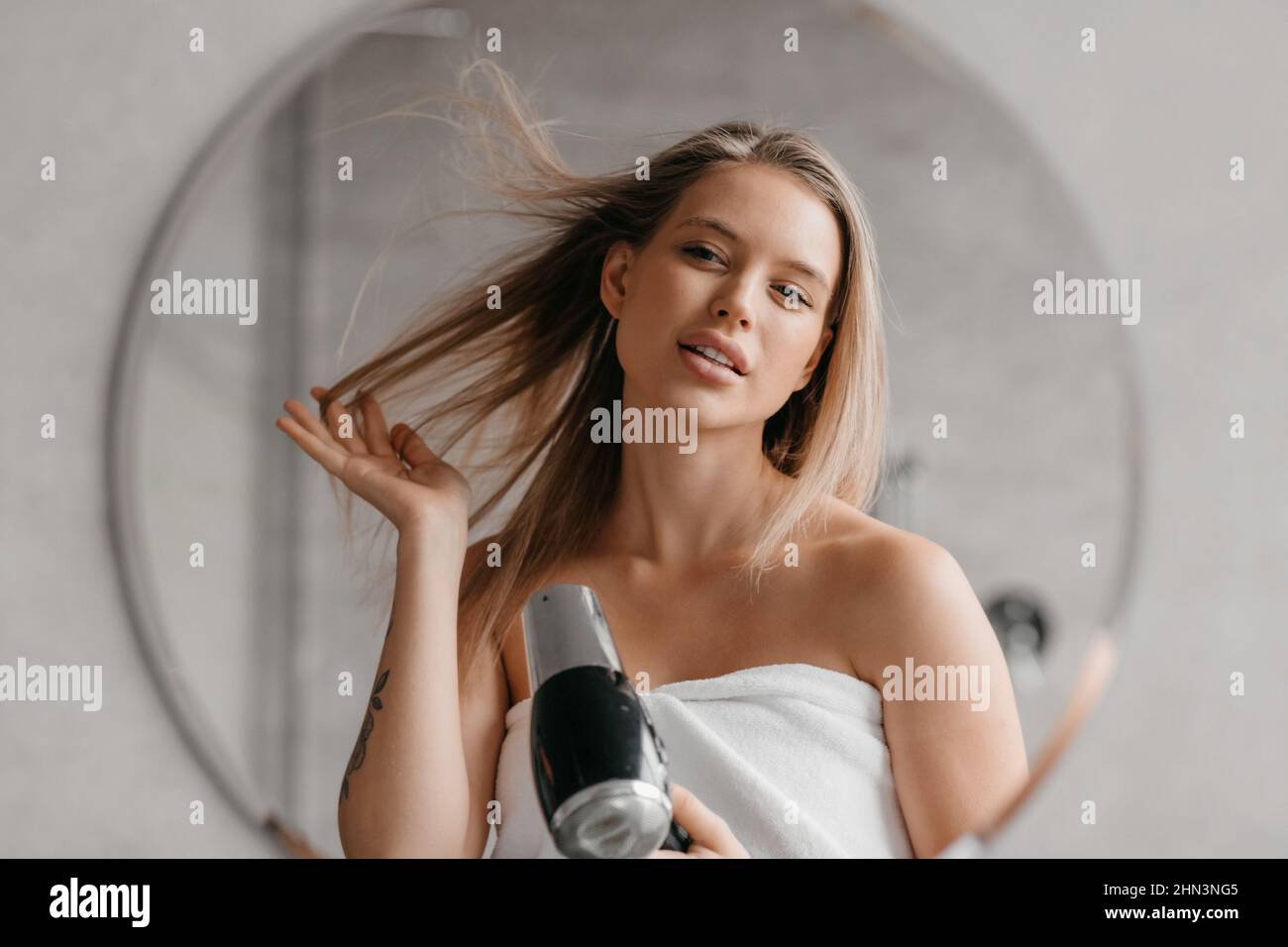 Haircare. Young woman drying and styling hair with hairdryer, making hairstyle after morning