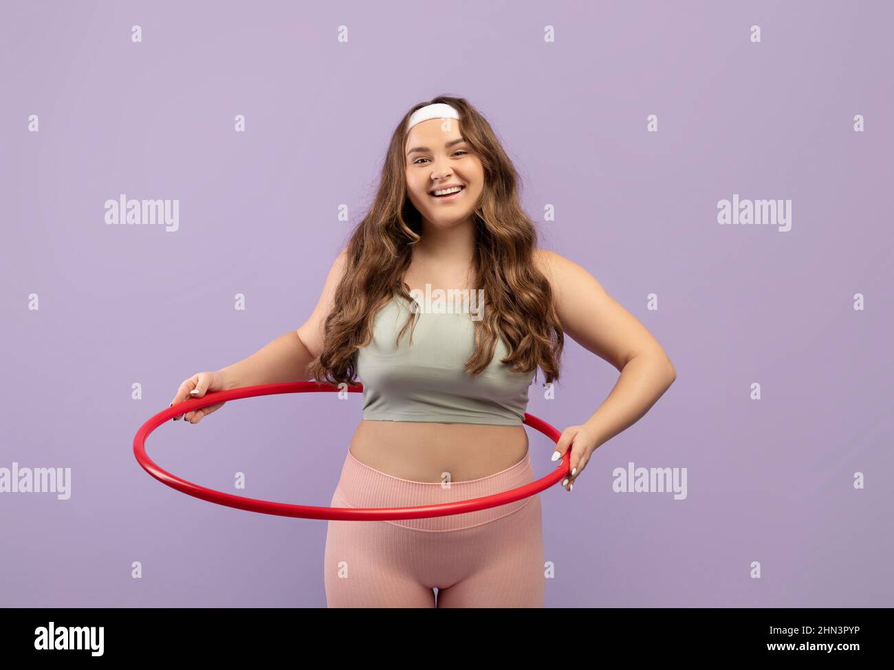 Smiling young european plus size female in uniform doing exercises with hula hoop Stock Photo