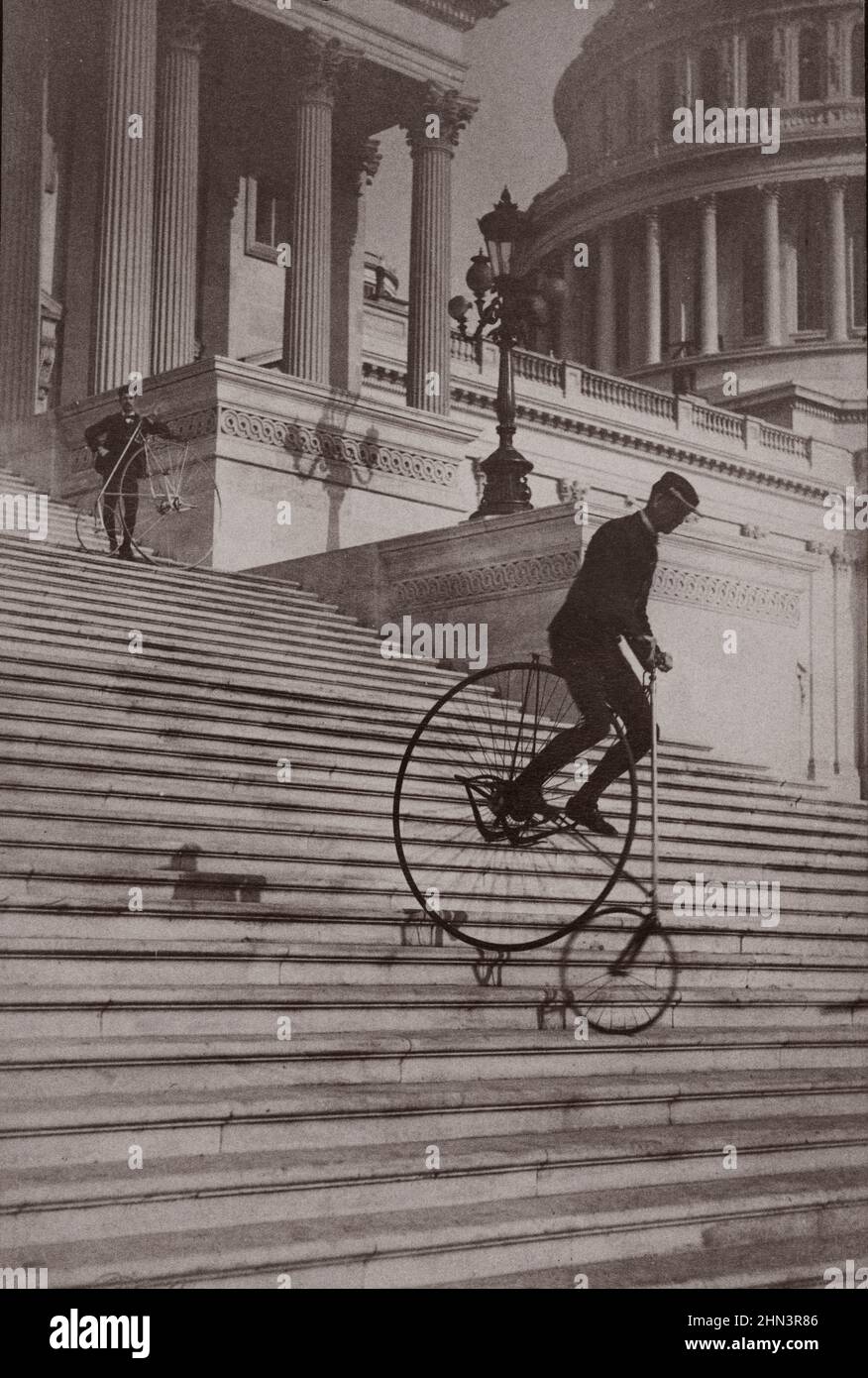 Vintage photograph shows a man riding a bicycle down the steps of the U.S. Capitol as another man with a bicycle waits at the top. 1884 Stock Photo