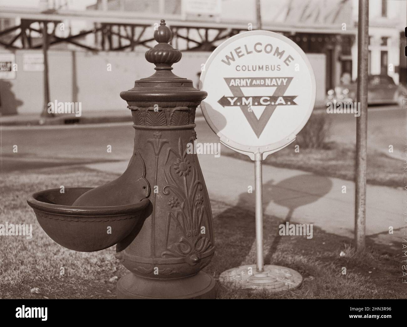 Vintage photo of American life in 1940s. Water trough and Y.M.C.A. (Young Mens Christian Association) welcome sign in square in center of town. Columb Stock Photo