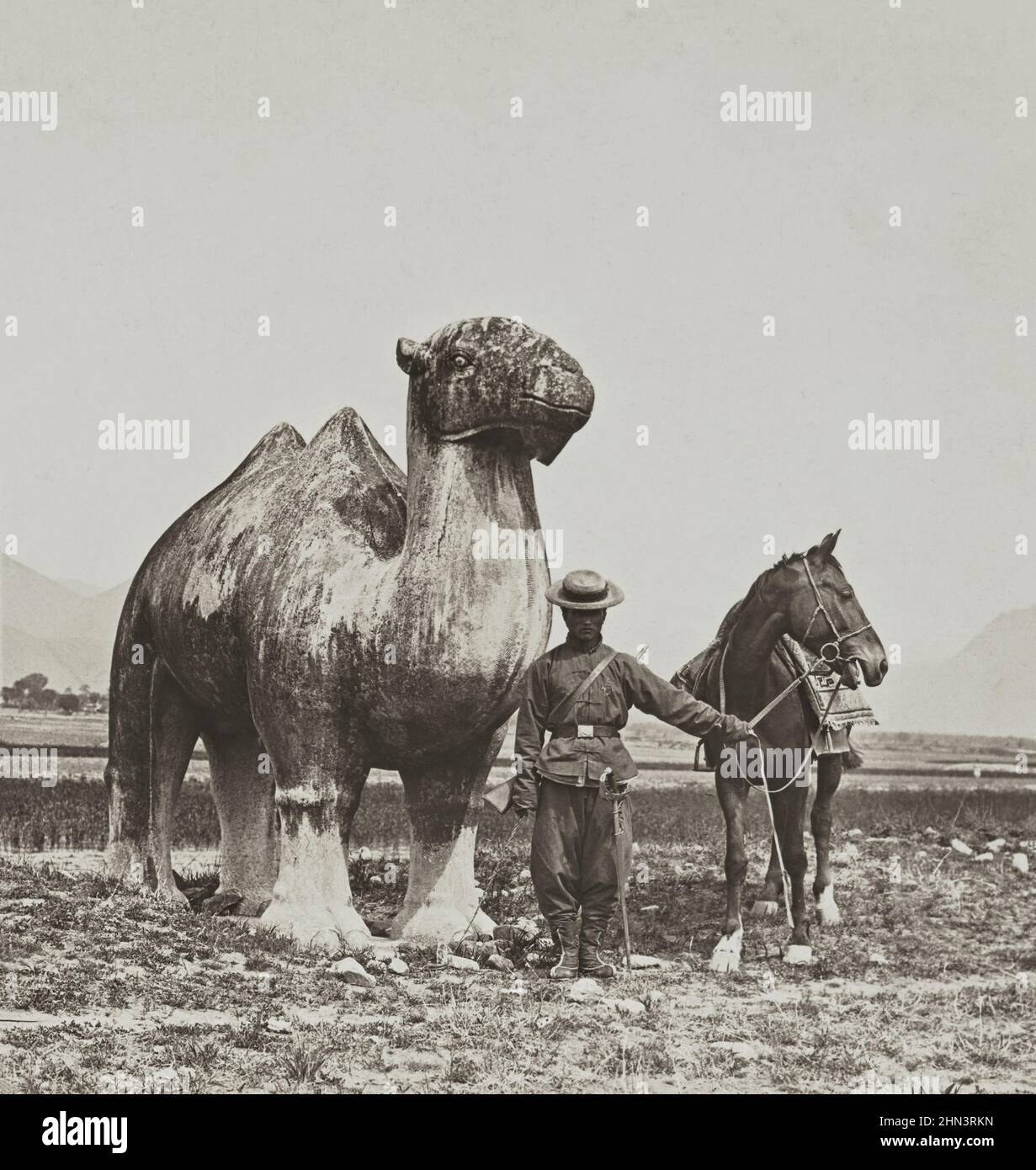 Vintagep photo of Qing Chinese soldier near ancient huge sculpture of stone camel. Ming Tombs. North China. November 1902 Stock Photo