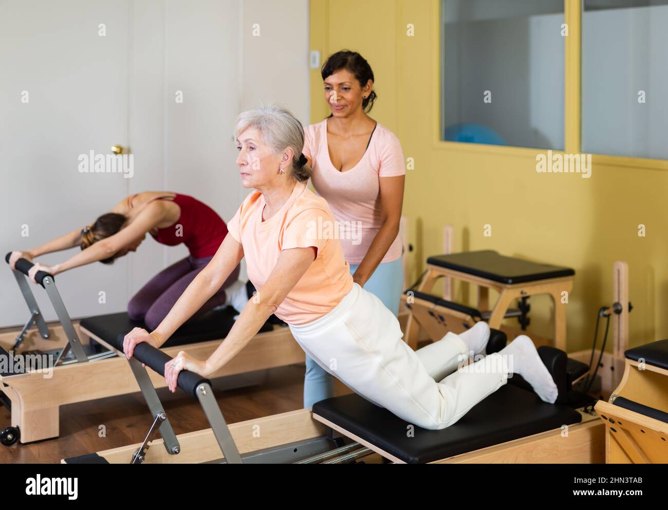 Pilates instructor assisting elderly woman to do exercises on reformer