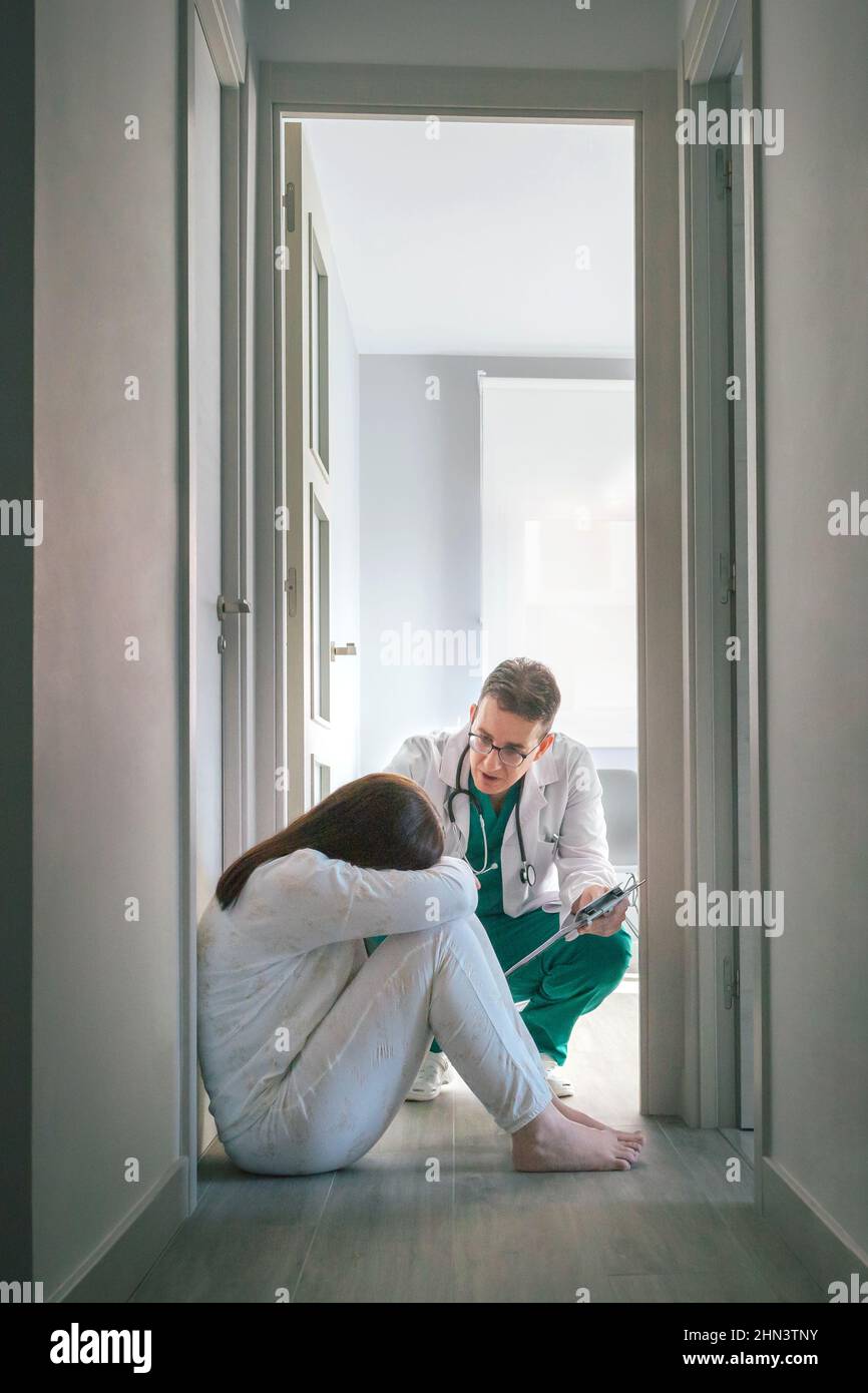 Psychiatrist talking to female patient with mental disorder sitting on the floor in a mental health center Stock Photo