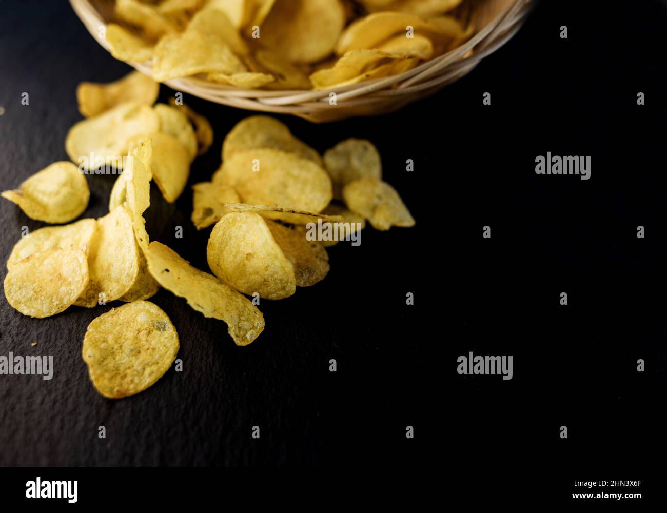 Crispy potato golden chips in a wicker bowl on dark background. unhealthy fatty food Stock Photo