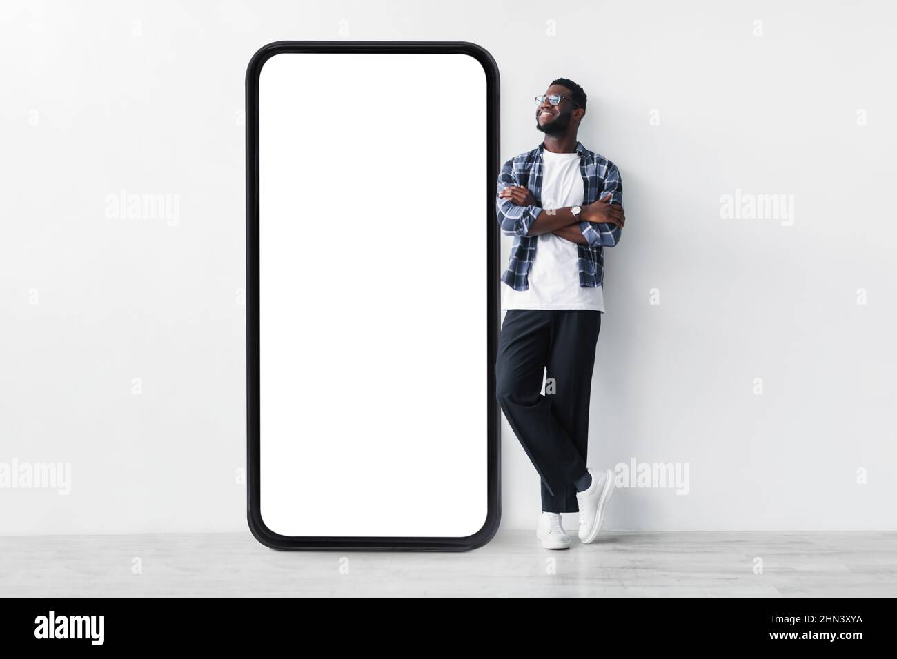 Full body length of black guy standing near huge giant smartphone with empty white screen template, mockup Stock Photo