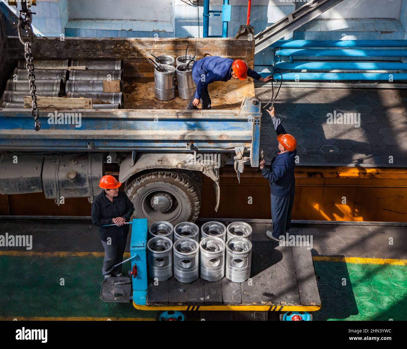Kazaly, Kazakhstan - May 02, 2012: Locomotive repair plant. Workers loading loco diesel engine pistons by the crane from truck to trolley. Stock Photo