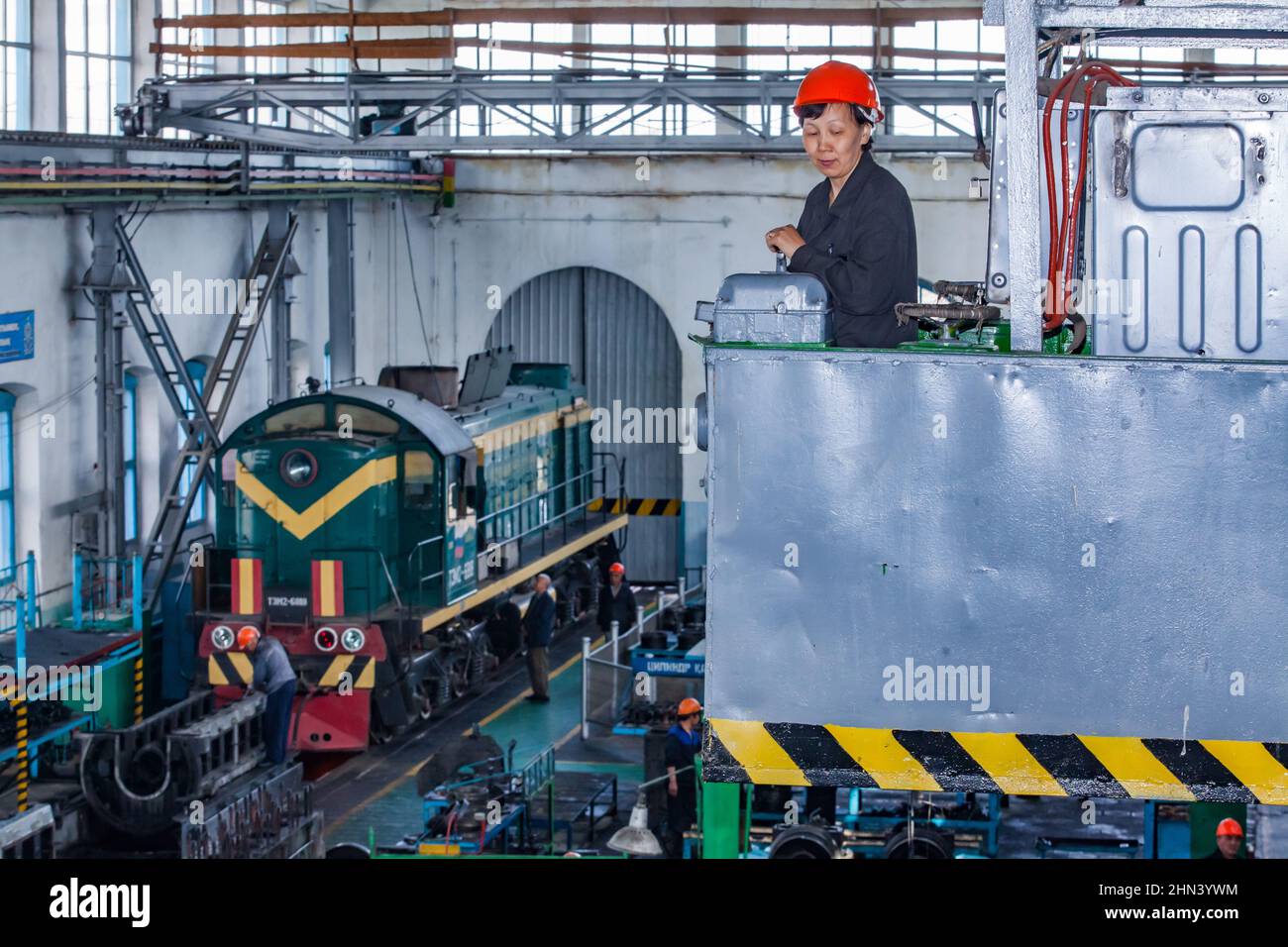 Kazaly, Kazakhstan - May 02, 2012: Locomotive repair plant. Asian woman crane operator in work. Diesel loco down left. Stock Photo