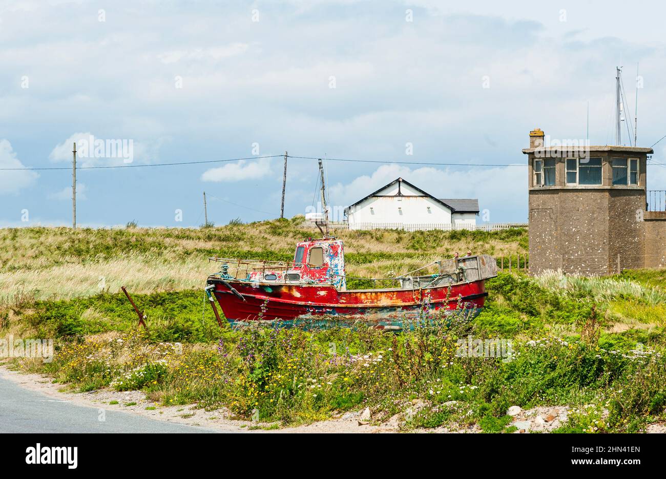 Red fisherman boat abandoned by a road. Forgotten, forsaken fishing trawler in the grass. Fishing dying business or industry. County Wexford, Ireland Stock Photo