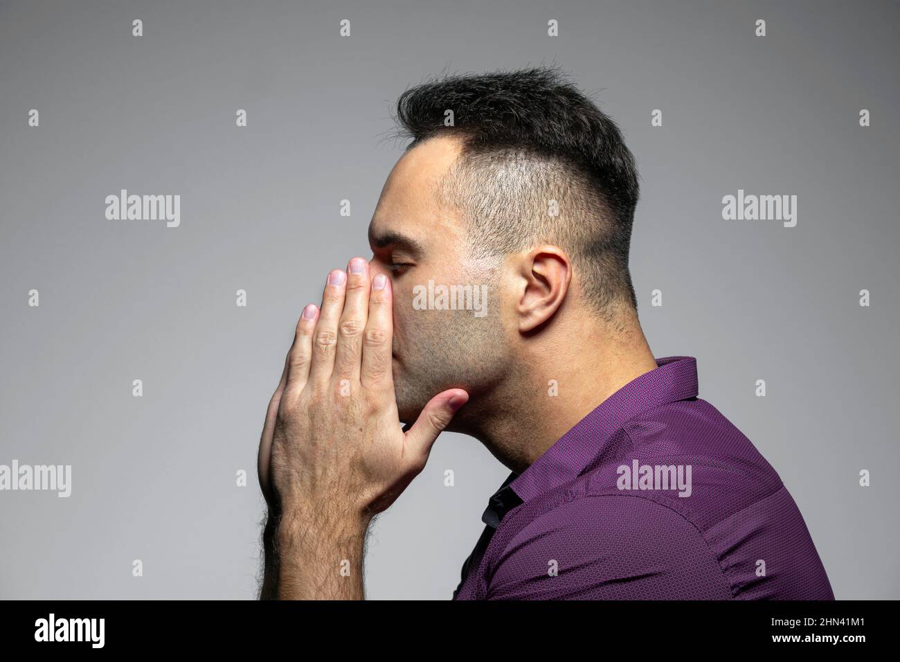 Profile portrait man with eyes closed and head in hands against gray background Stock Photo