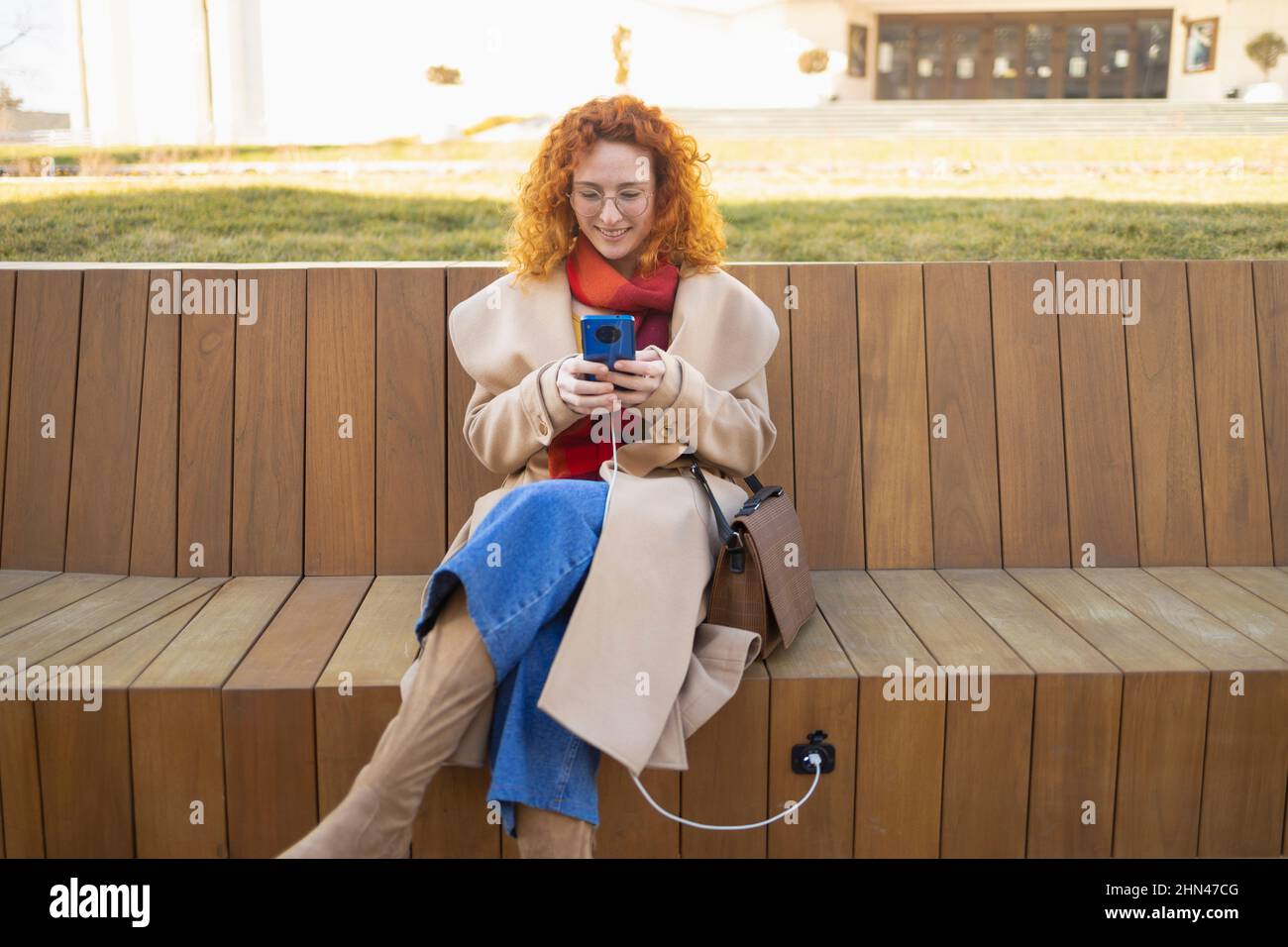 Young woman using her smartphone on a smart bench in a modern city Stock Photo