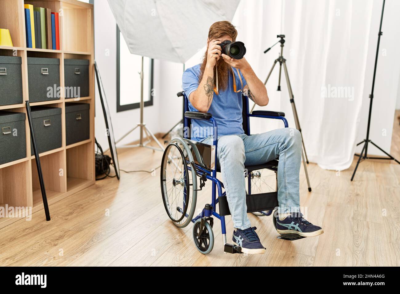 Young redhead man photographer sitting on wheelchair using professional camera at clinic Stock Photo