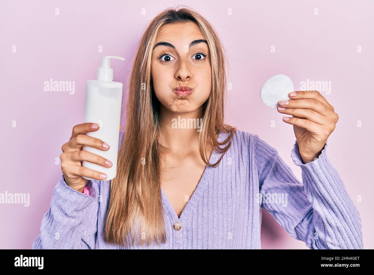 Beautiful hispanic woman holding cotton pad and make up remover puffing cheeks with funny face. mouth inflated with air, catching air. Stock Photo