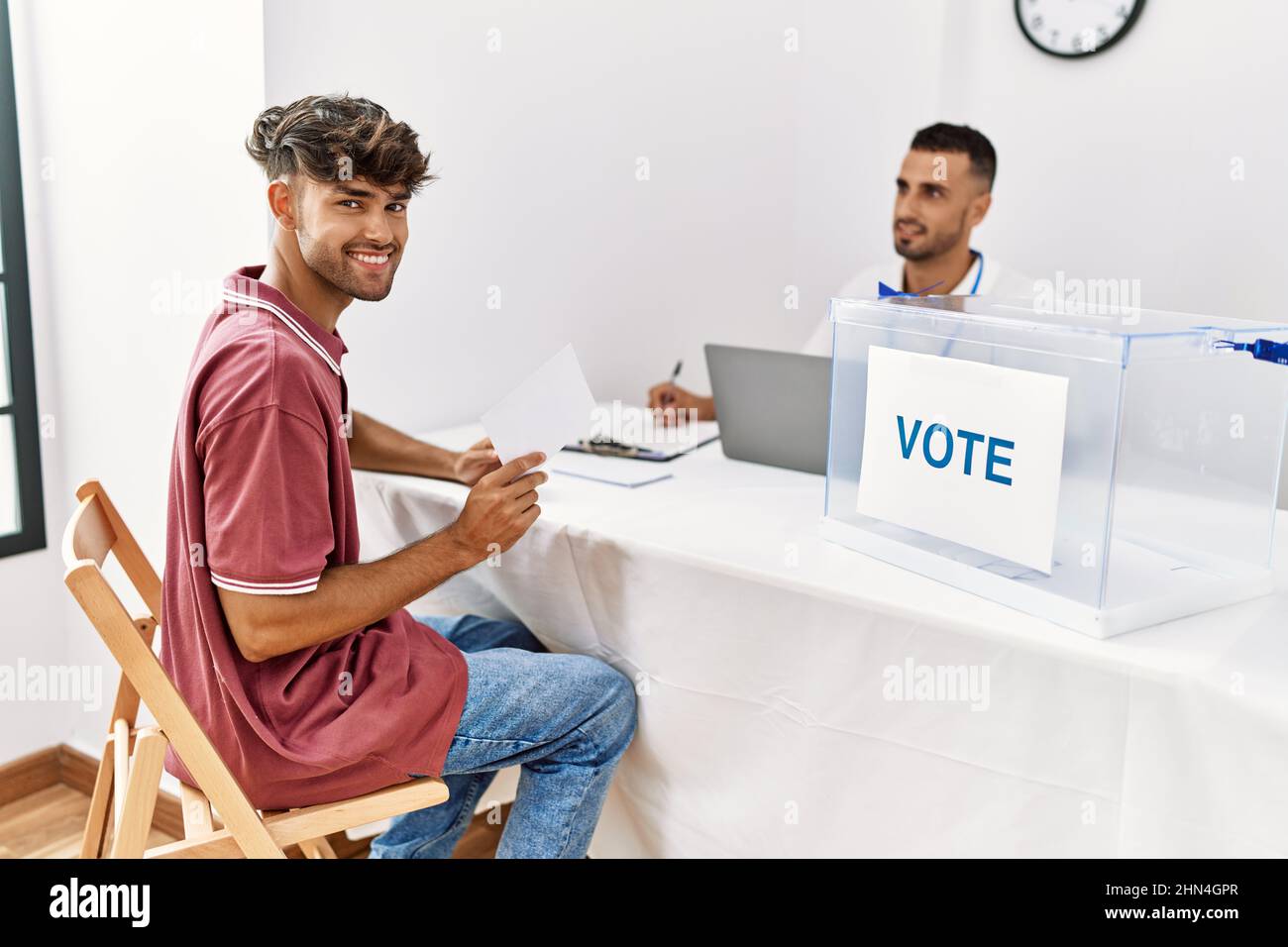 Young hispanic voter man smiling happy holding vote at electoral center. Stock Photo