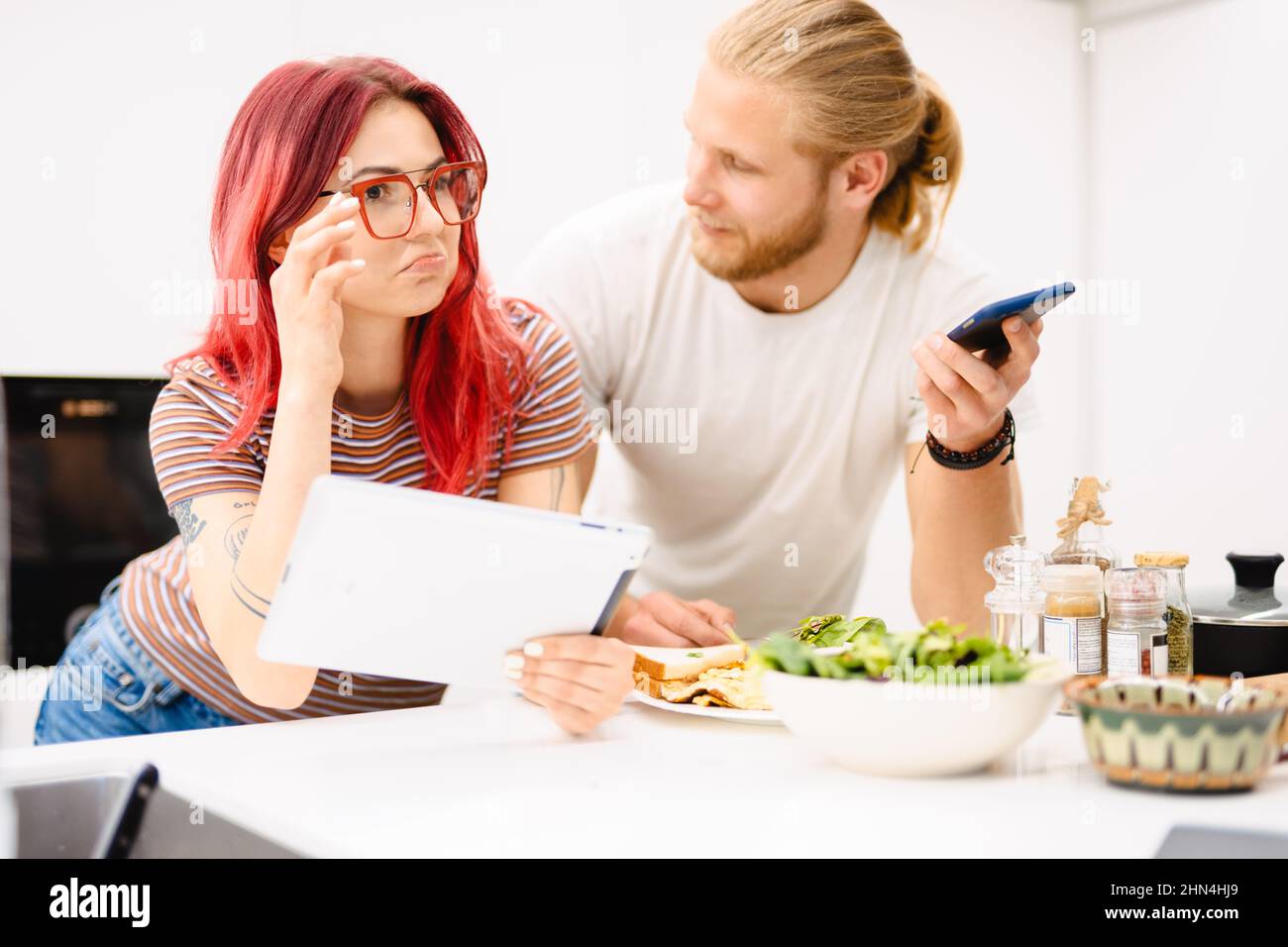 https://c8.alamy.com/comp/2HN4HJ9/young-white-couple-using-gadgets-while-having-lunch-in-kitchen-at-home-2HN4HJ9.jpg