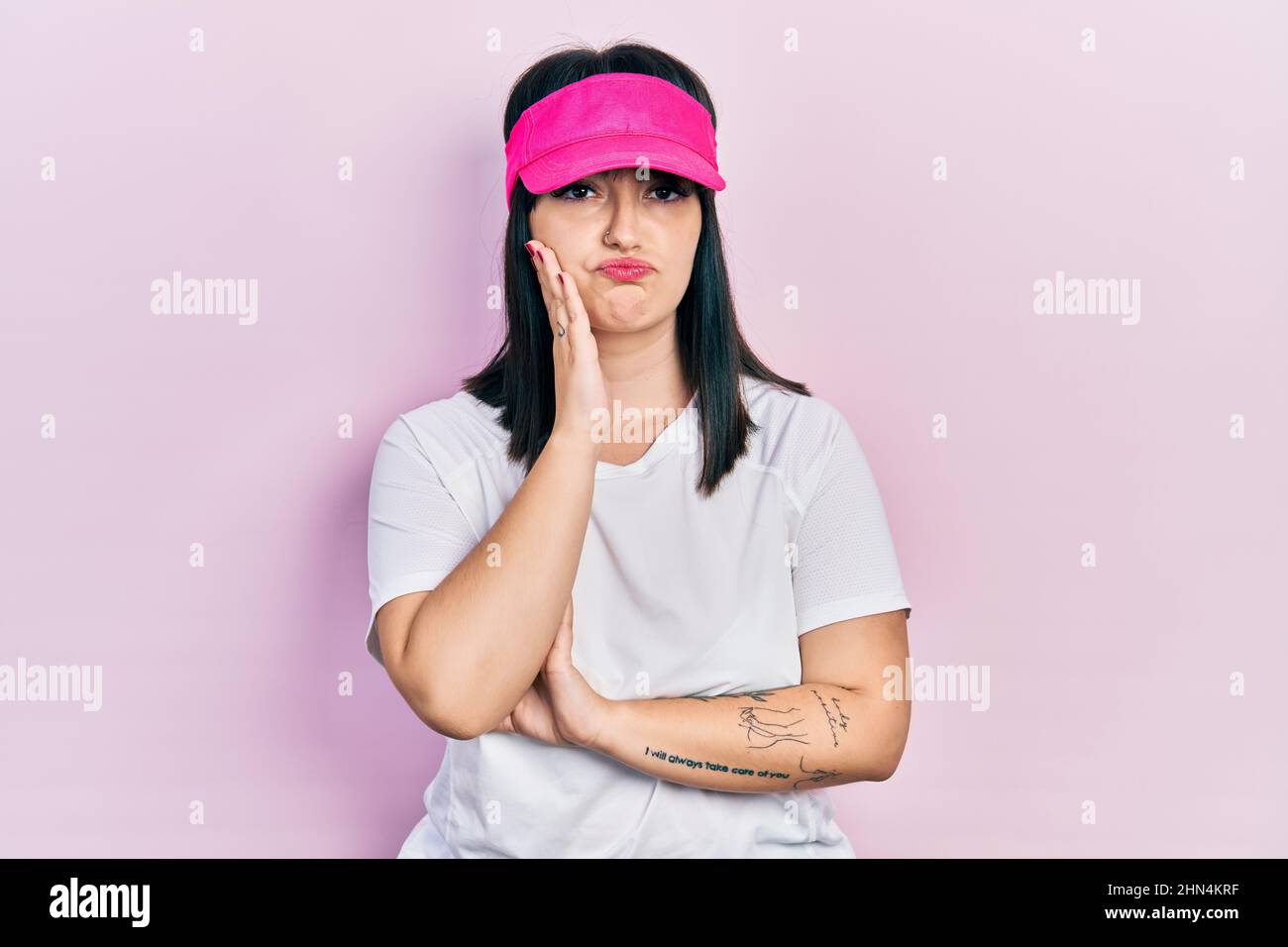 Young hispanic woman wearing sportswear and sun visor cap thinking looking tired and bored with depression problems with crossed arms. Stock Photo