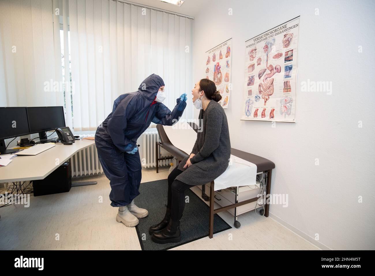 Vechta, Germany. 11th Feb, 2022. In a posed situation, Alina Schillmöller  (l), dressed in a protective suit, takes a swab from Janine Pahlke (r) in  an examination room of the health department