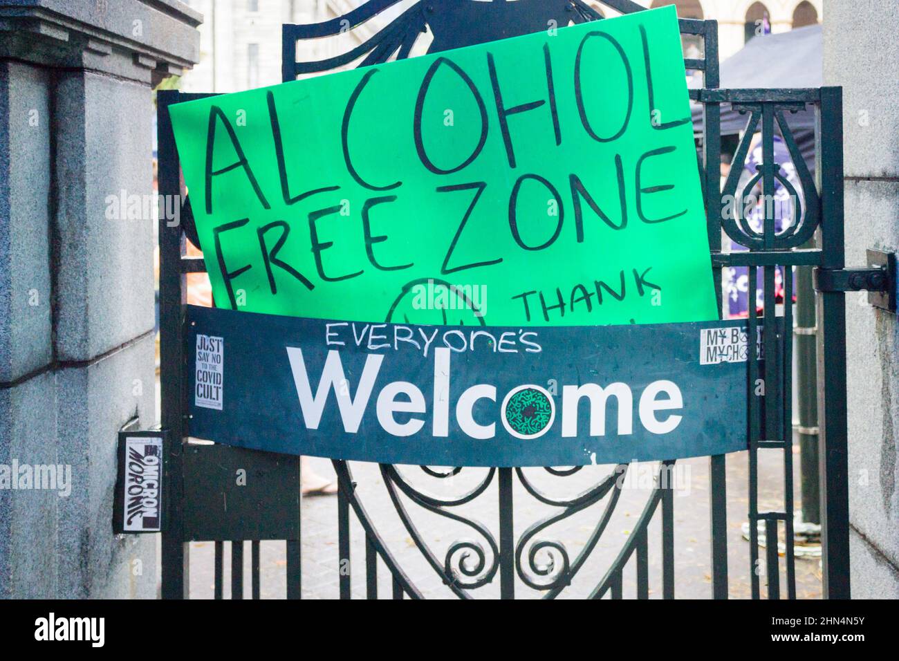 Wellington, New Zealand. February 13, 2022:  A Welcome sign on the gates of Parliament with a protestor's placard declaring an alcohol free zone. Stock Photo