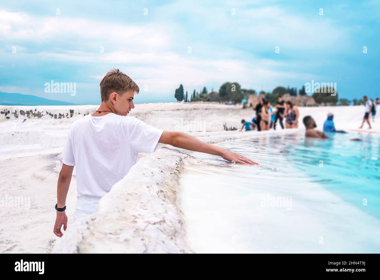Cute teenager aged 15-18 reached out his hand and touched the water in the travertine pool in Pamukkale. Stock Photo
