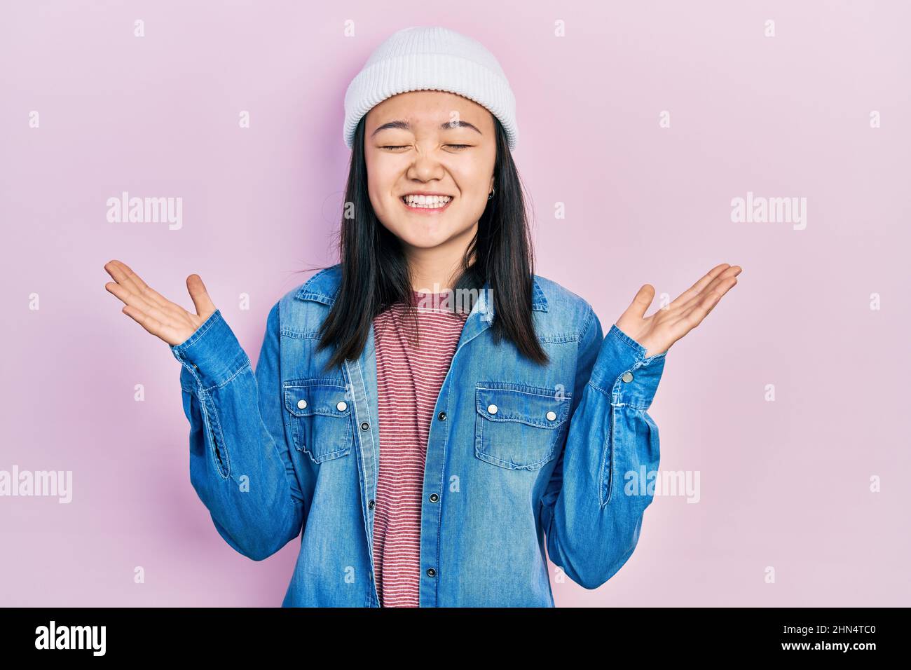 Young chinese girl wearing cute wool cap celebrating mad and crazy for success with arms raised and closed eyes screaming excited. winner concept Stock Photo