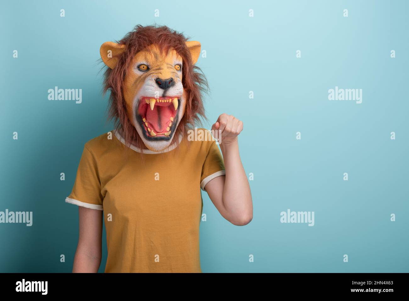 Young woman in lion mask hold raised hand for fist bump, isolated on blue background with copy-space. Stock Photo