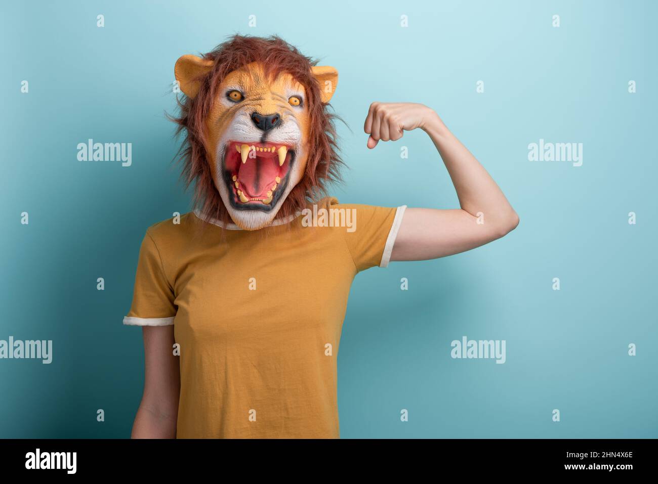 Young woman in lion mask flexing arm muscles, isolated on blue background  with copy-space Stock Photo - Alamy