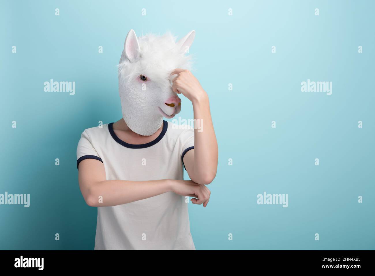 Young woman in alpaca mask scratching her head, thinking or in doubt, isolated on blue background with copy-space. Stock Photo