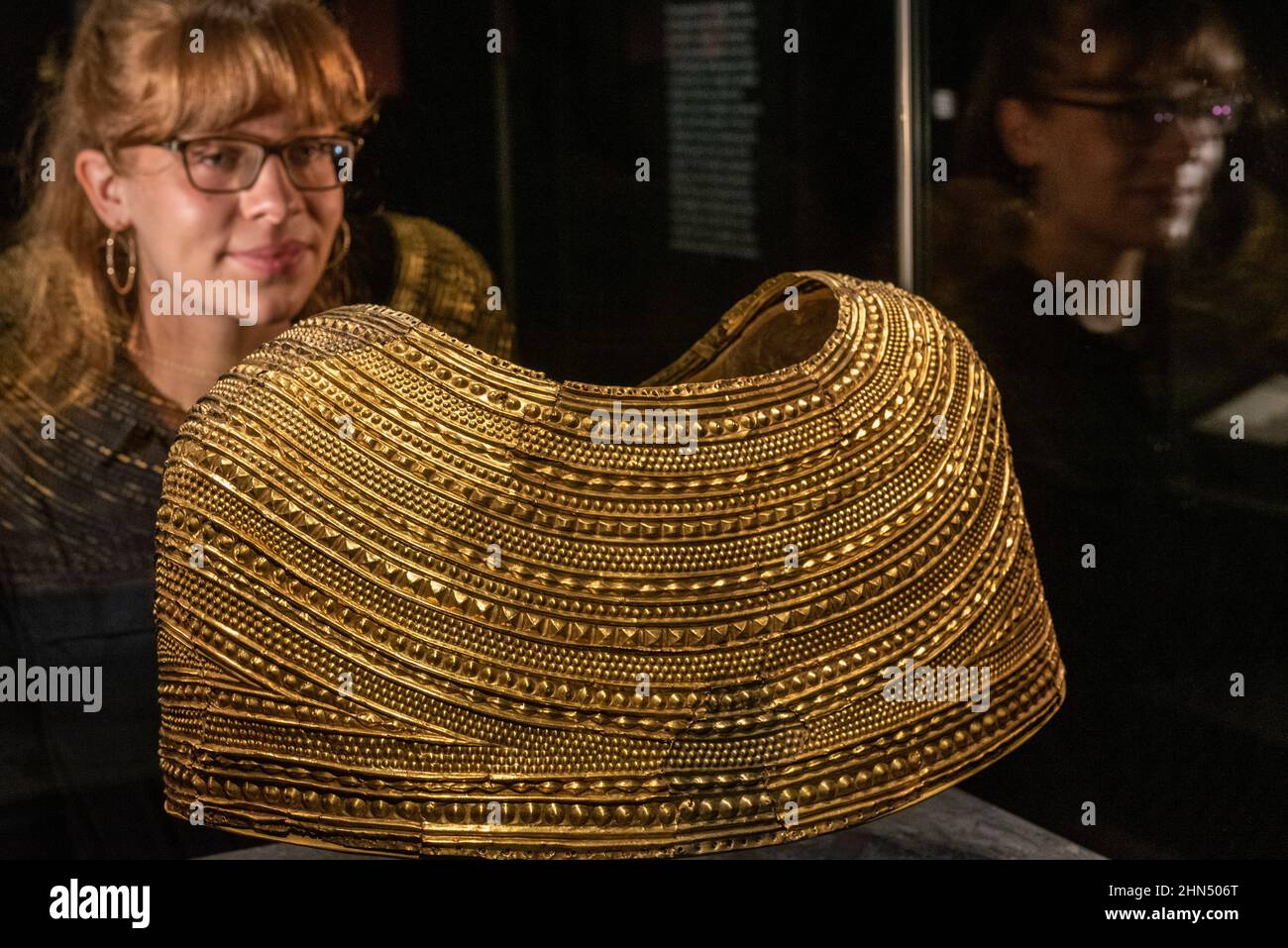 London, UK.  14 February 2022. A staff member poses with a gold cape from Mold in Wales, about 1900-1600 BC. Preview of “The world of Stonehenge” at the British Museum”, the UK’s first ever major exhibition on Stonehenge which features over 430 objects on show from Britain, Ireland and Europe.  The works are on display 17 February to 17 July 2022.  Credit: Stephen Chung / Alamy Live News Stock Photo