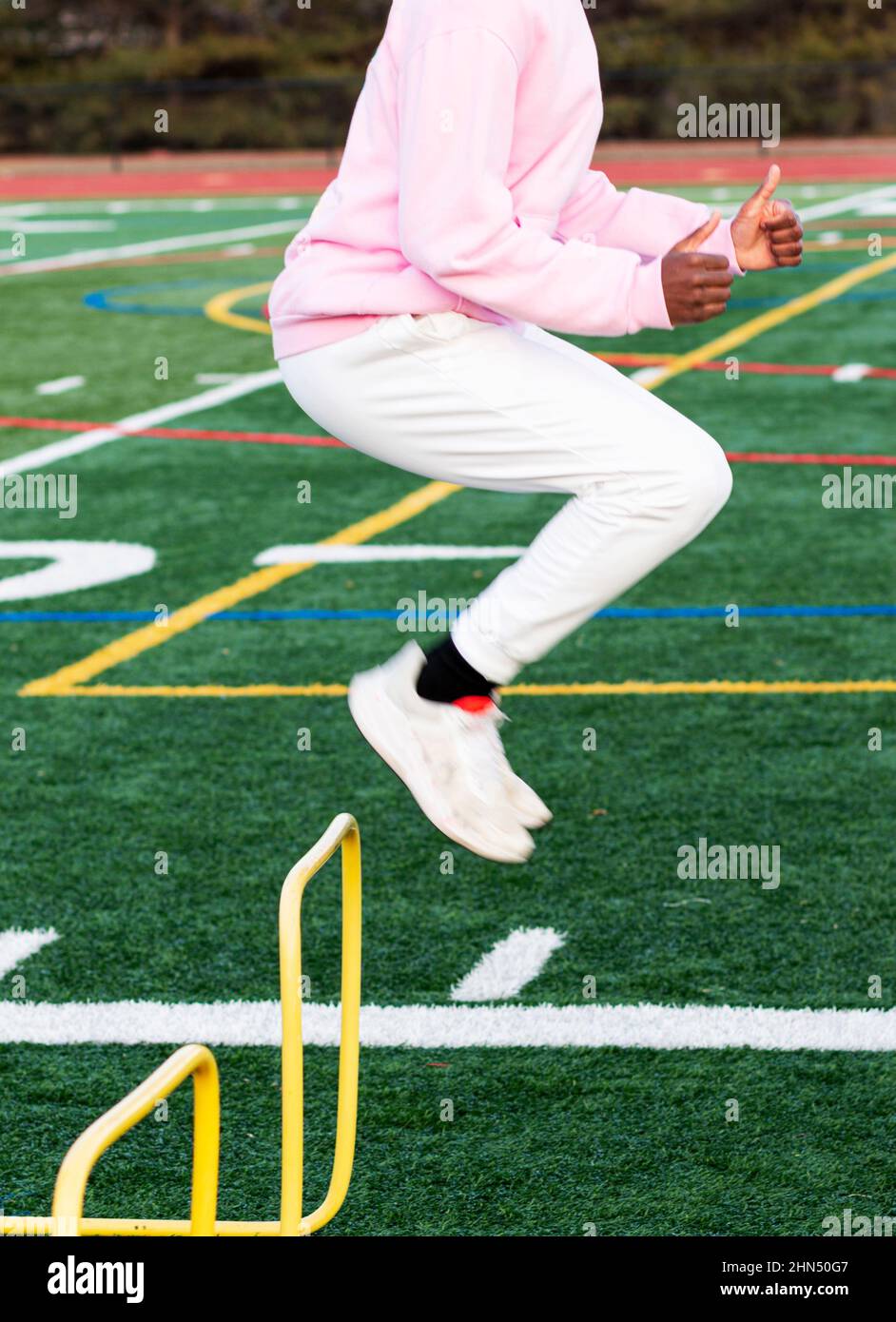 Rear view of a high school track runner jumping over plastice yellow