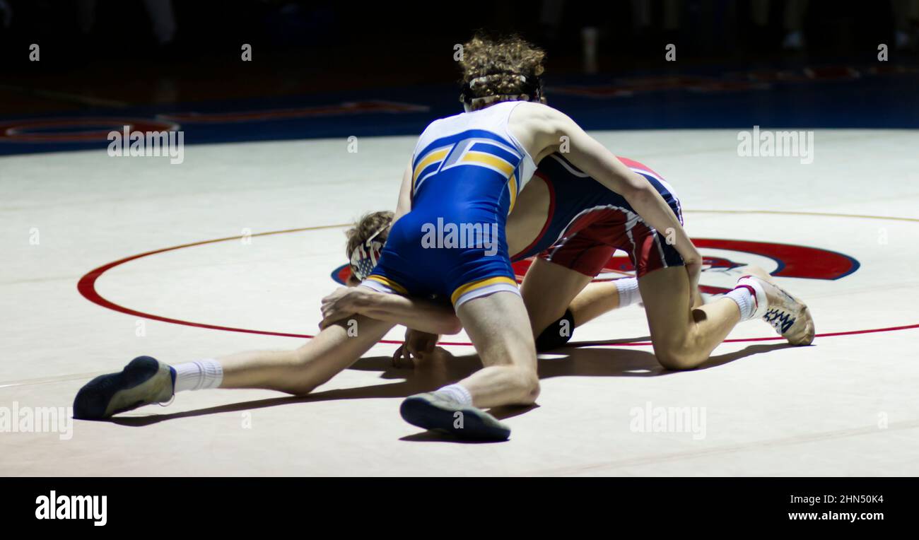 Two high school wrestlers wrestling during a match under a spot light
