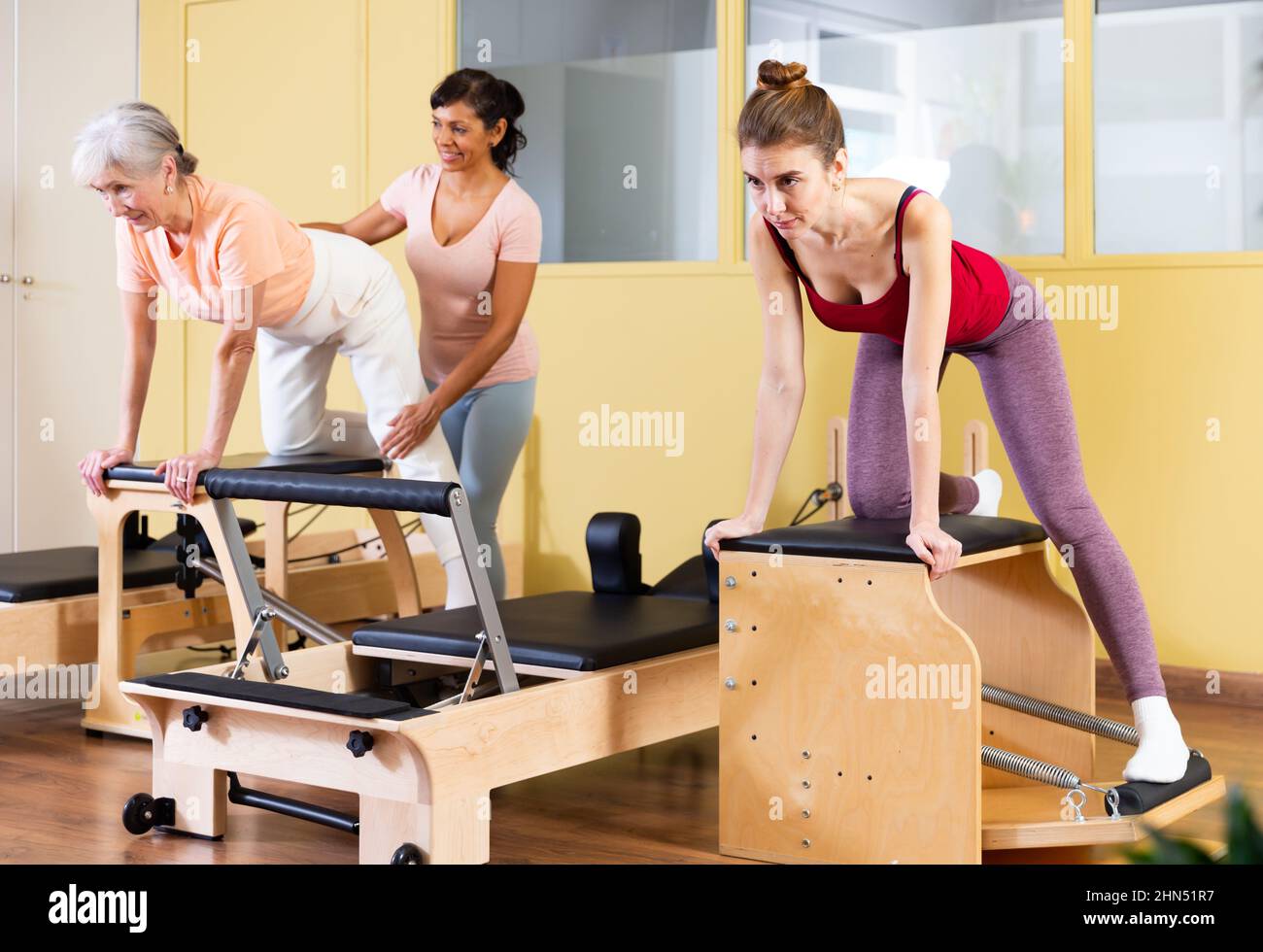 Female instructor helps women perform an exercise on a combined chair